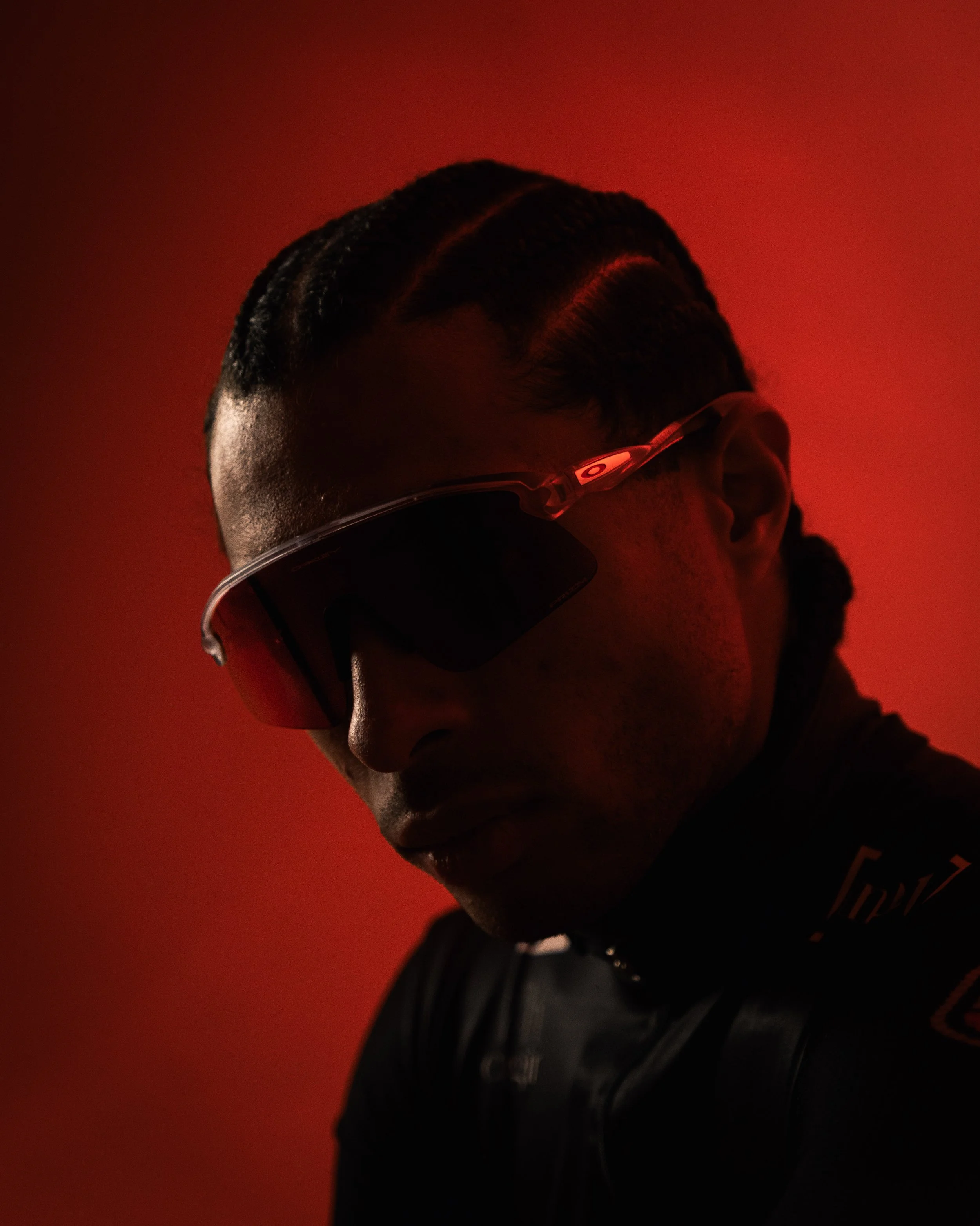 Person with styled hair wearing sunglasses and a black shirt, with a red background.