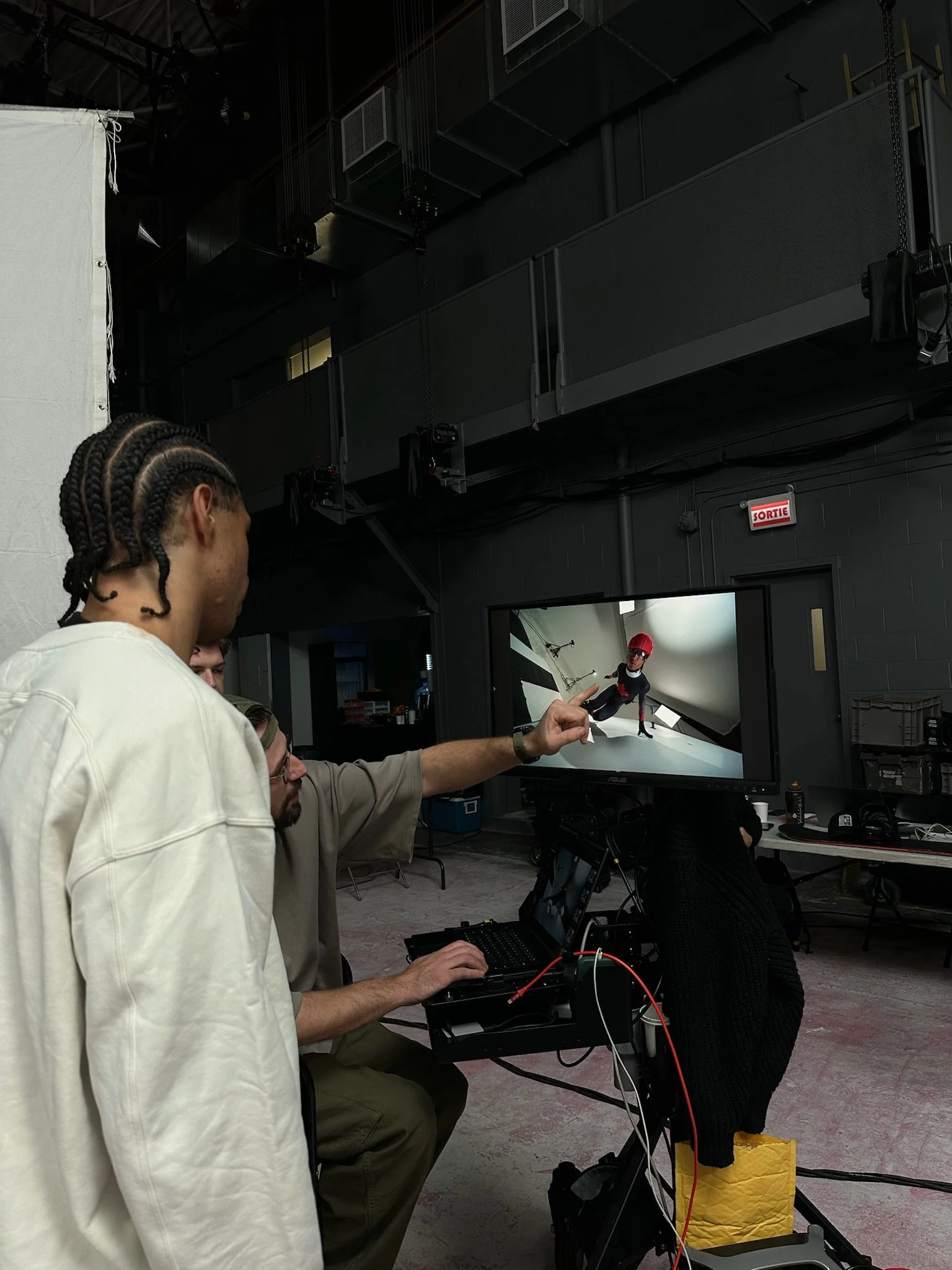 People in a studio or control room watching a monitor displaying a puppet show or performance, with members of the crew working with equipment and computers.