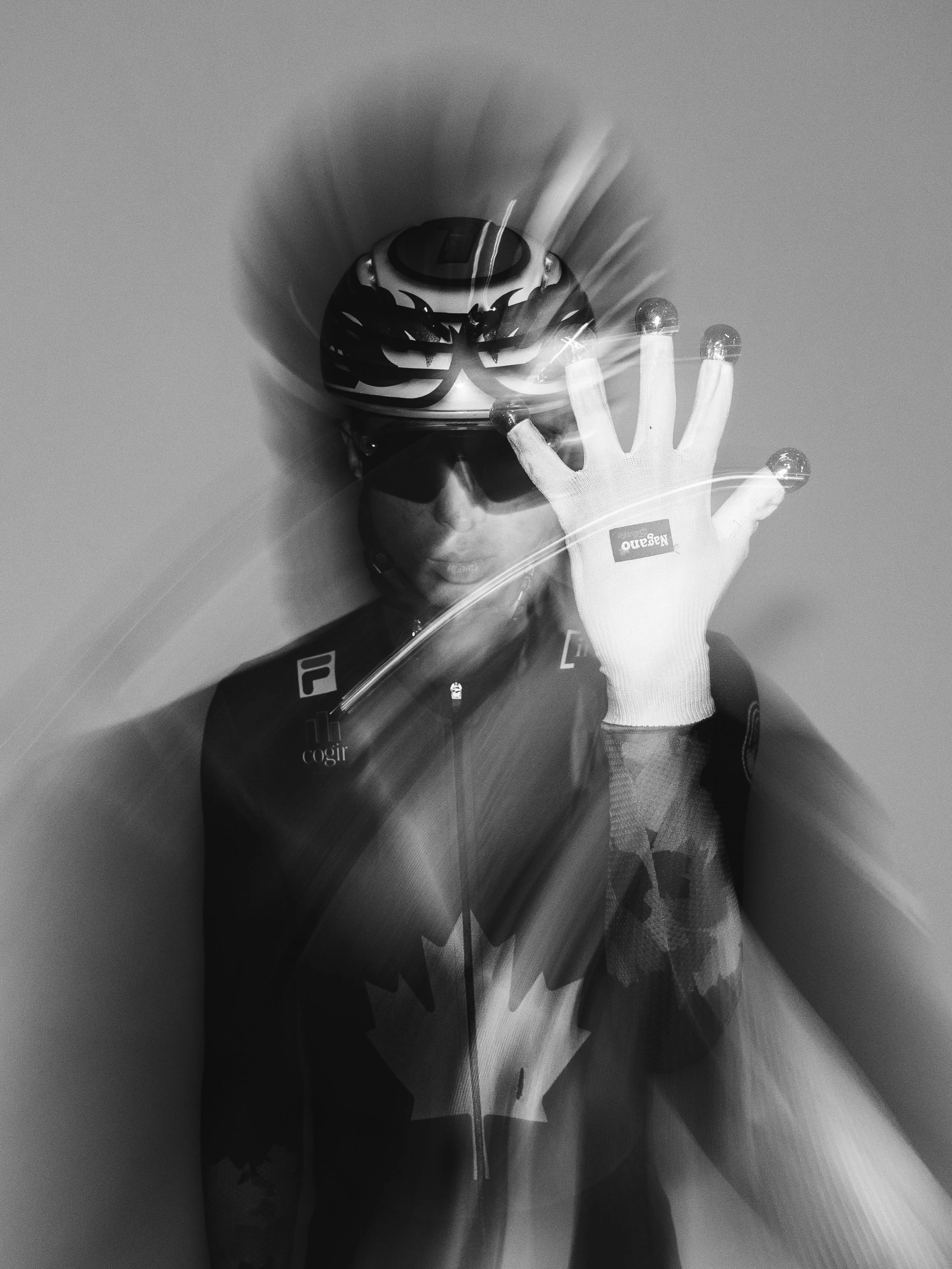 A person wearing a motorcycle helmet with graphic designs and sunglasses, holding a small light-emitting object in their gloved hand, with motion blur effects in the image.