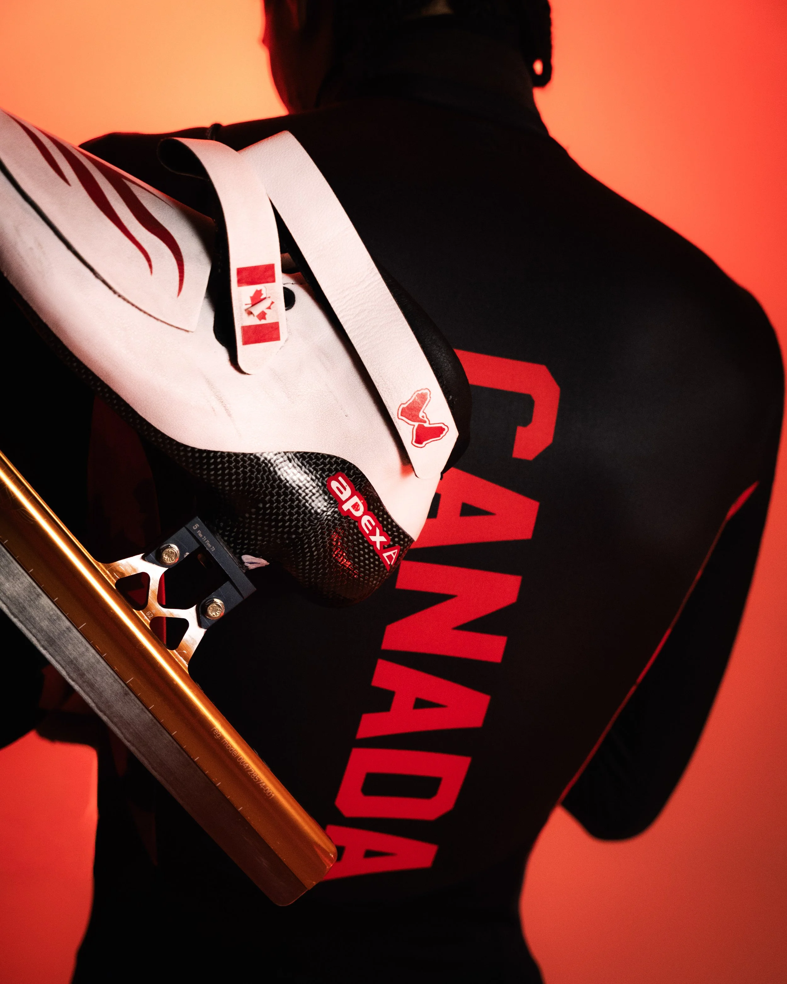 Close-up of a person wearing a black shirt with red text, holding a hockey stick with a white and black grip, against a red background.