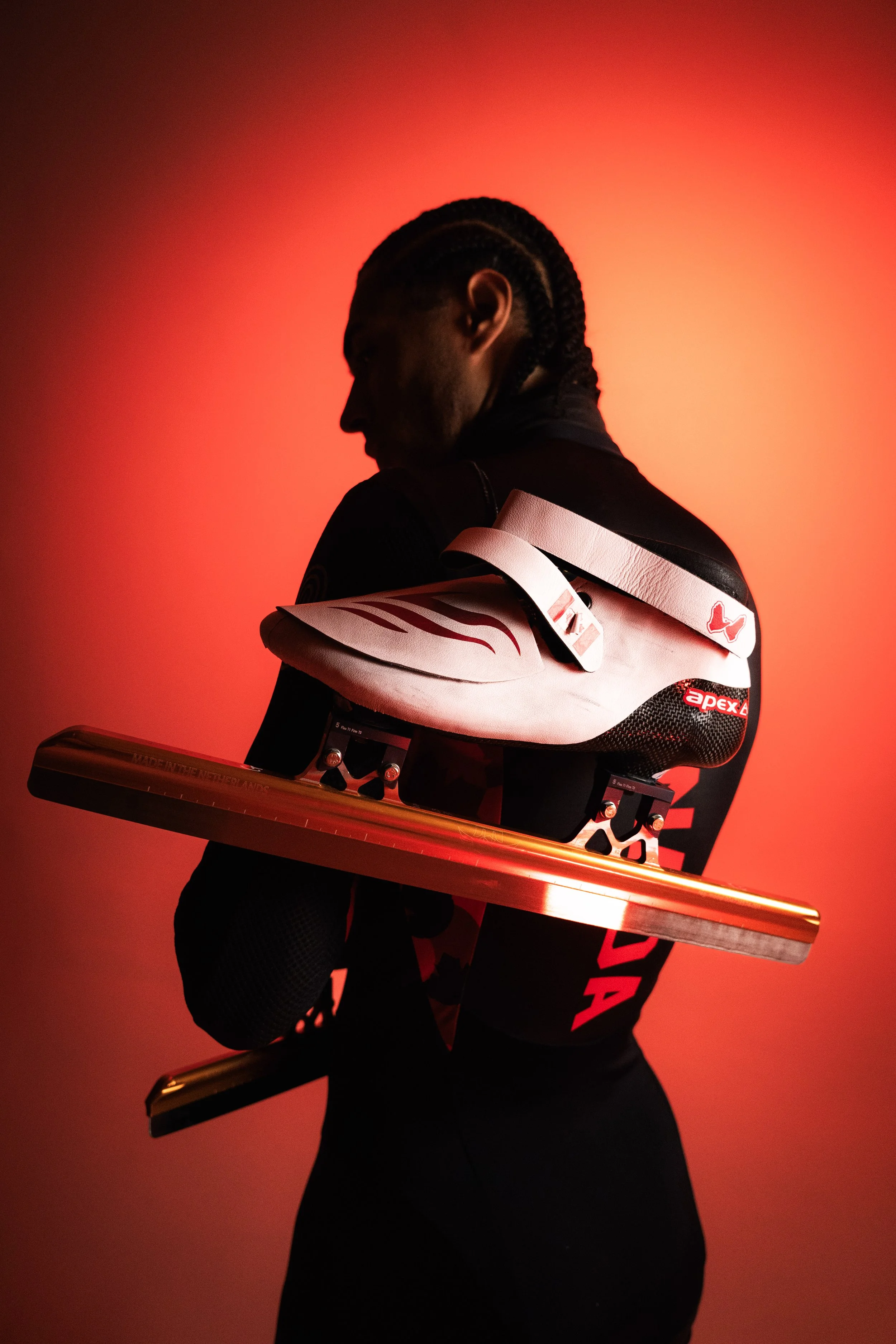 Silhouette of a person with cornrows holding a skateboard against a red background.