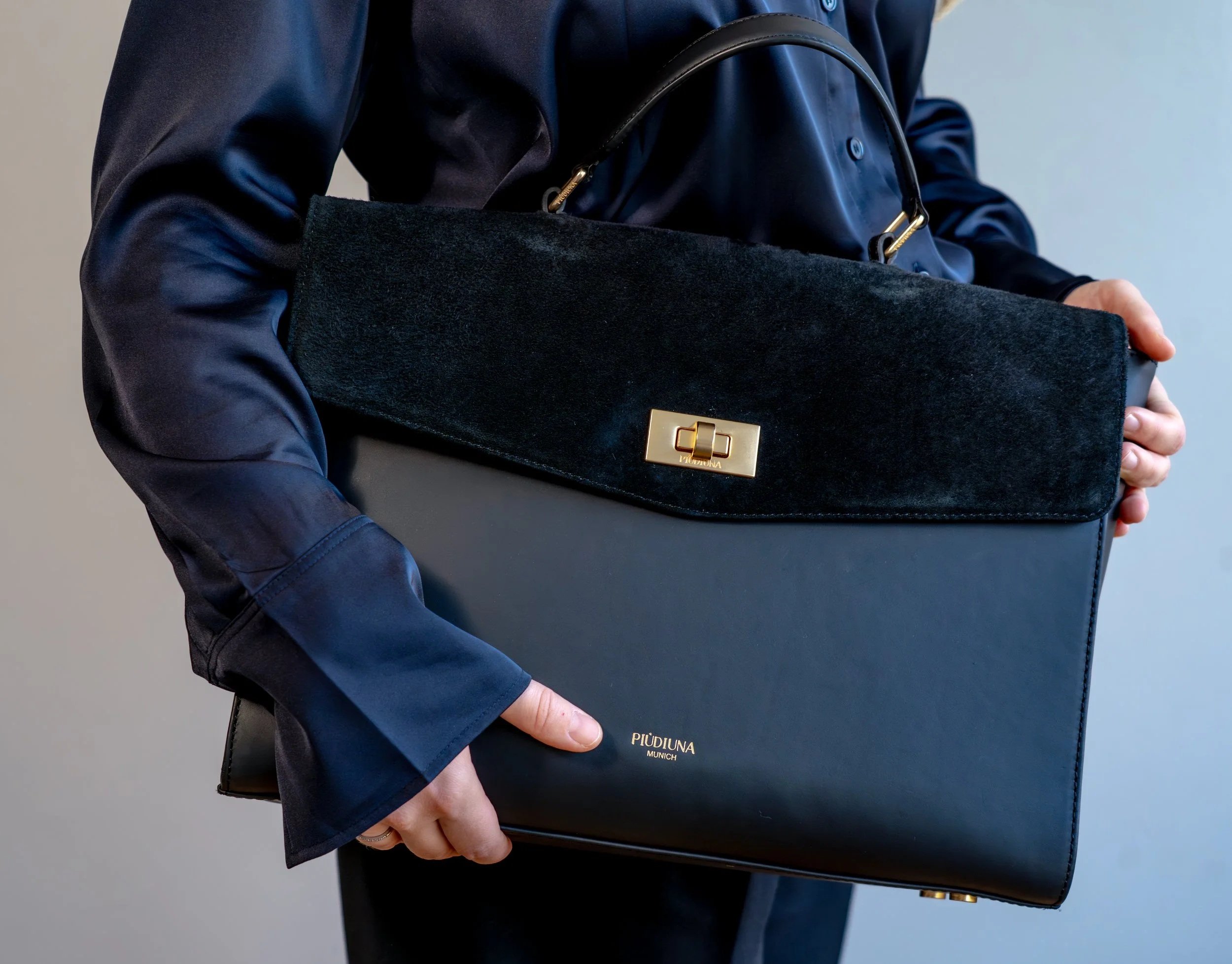 Person hält eine schwarze Handtasche mit goldener Schnalle, trägt dunkle Kleidung und legt eine Hand in die Tasche.
