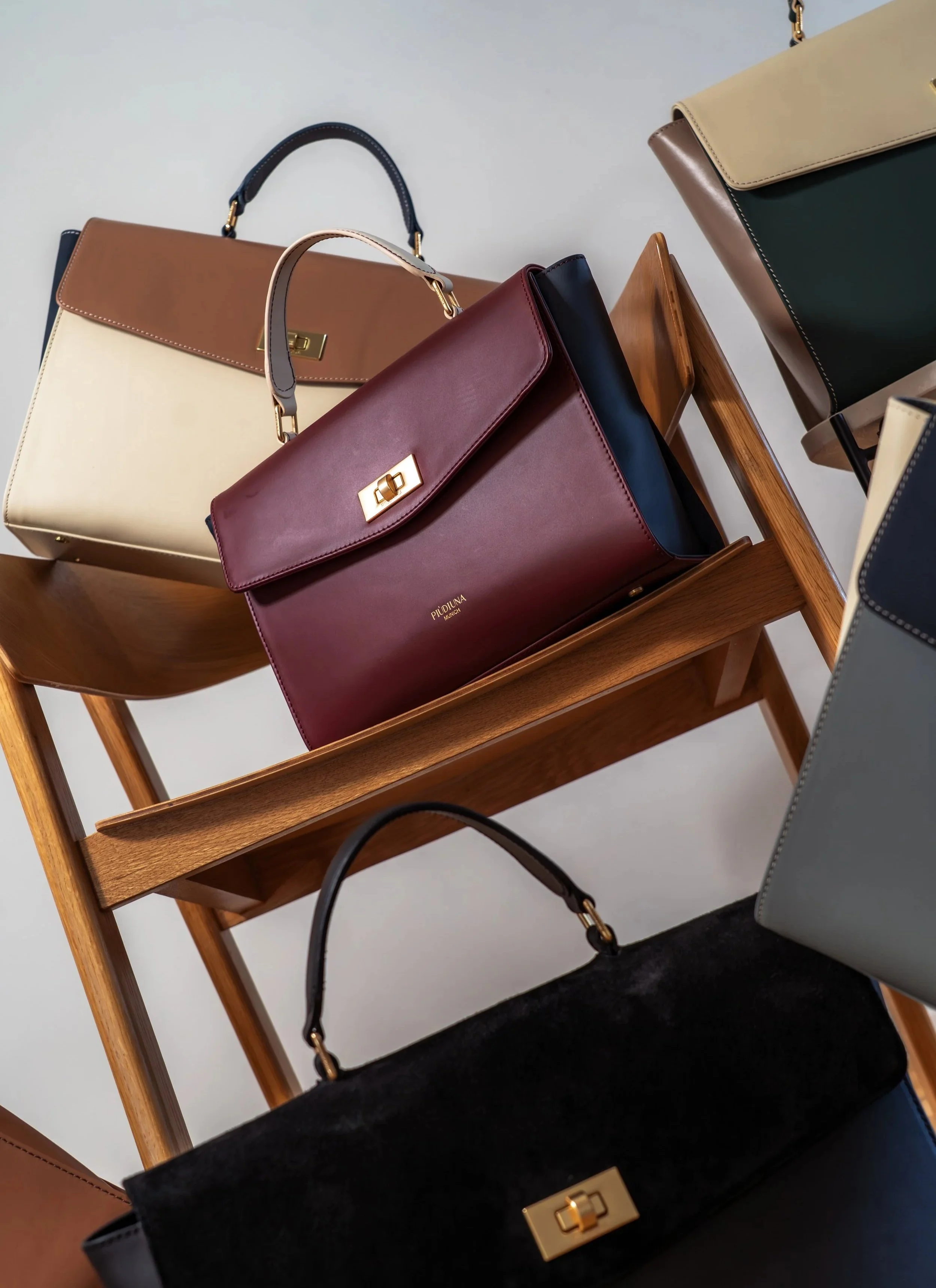 Verschiedene elegante Handtaschen in unterschiedlichen Farben auf einem Holzstuhl.
