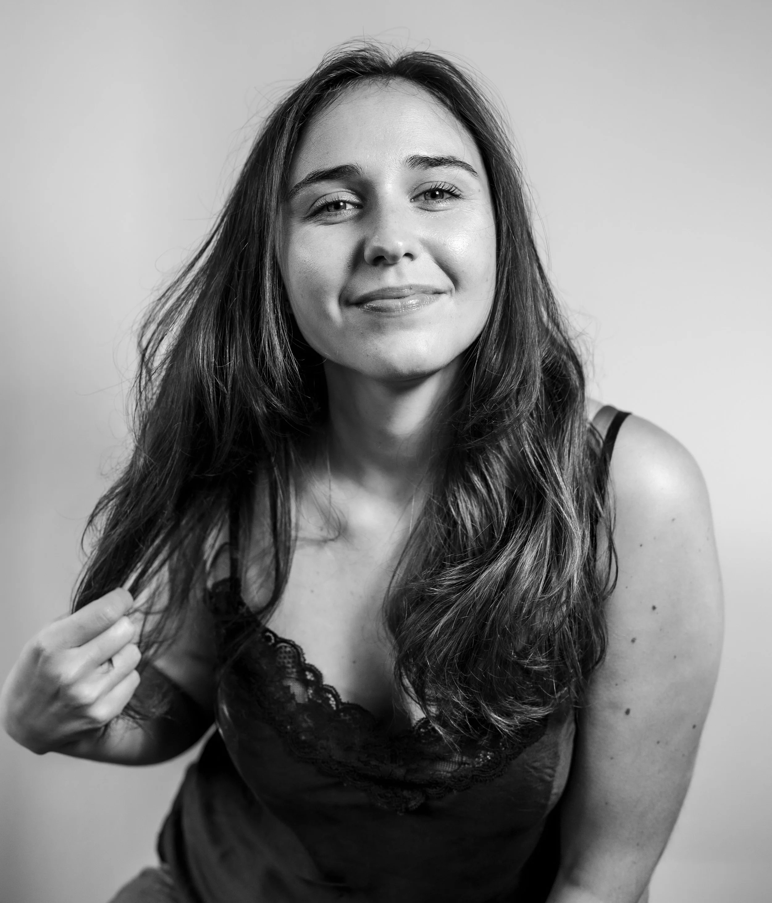 Schwarz-weiß-Foto einer jungen Frau mit langen, lockigen Haaren, die an einem schwarzen Spitzenkleid zu sehen ist, während sie an ihrem Haar fasst.