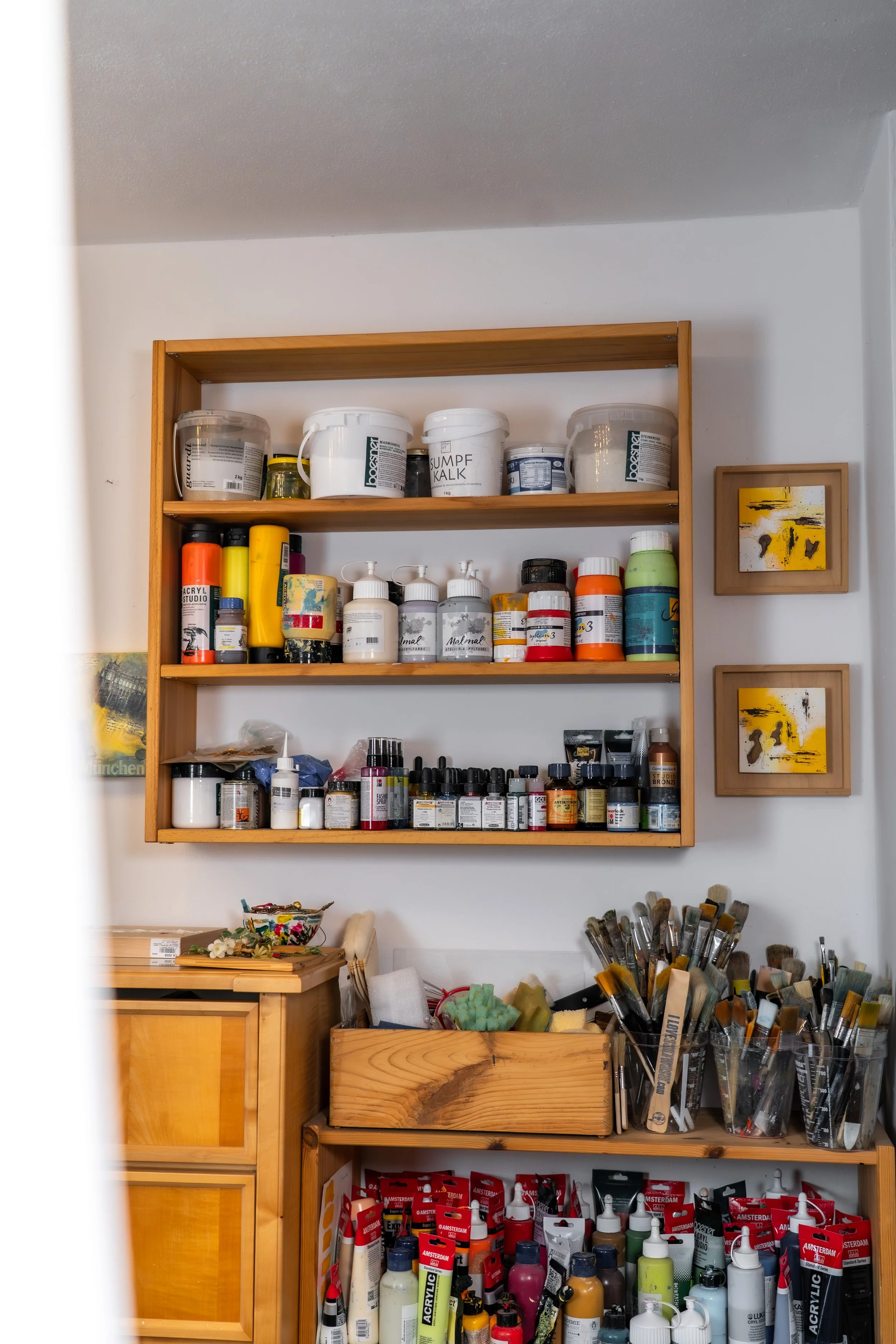 Ein Holzregal mit Malutensilien wie Farben, Pinseln, Modeliermasse und Acrylfarben in einer Kunstwerkstatt.