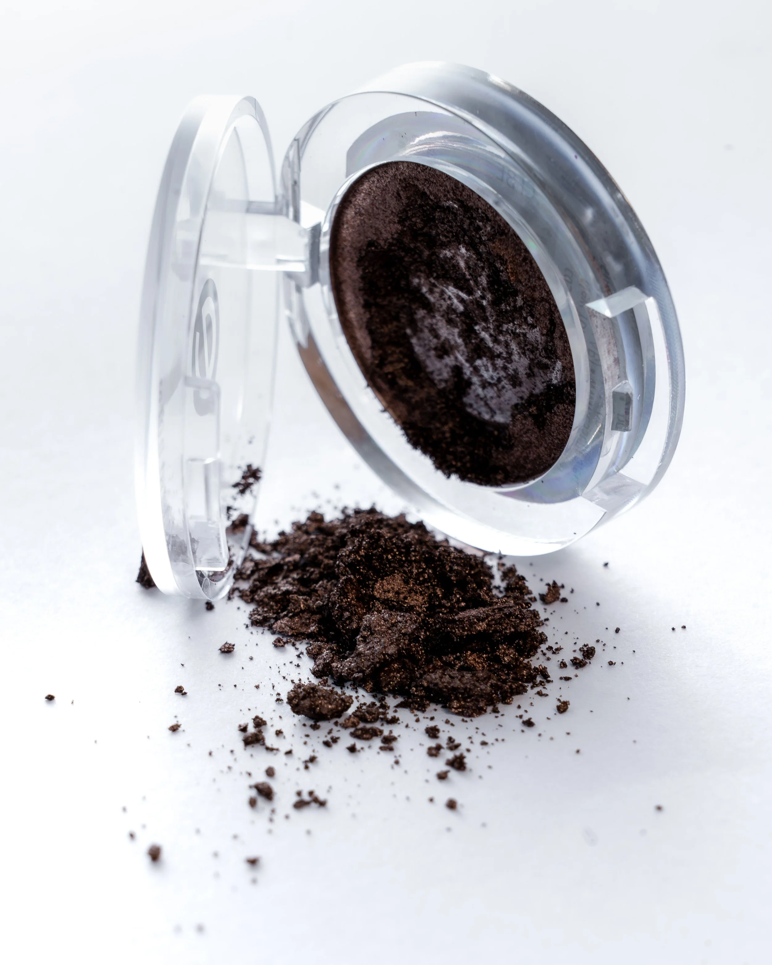 Eine offene Dose mit Kaffeepulver, aus der Pulver auf eine weiße Oberfläche fällt.