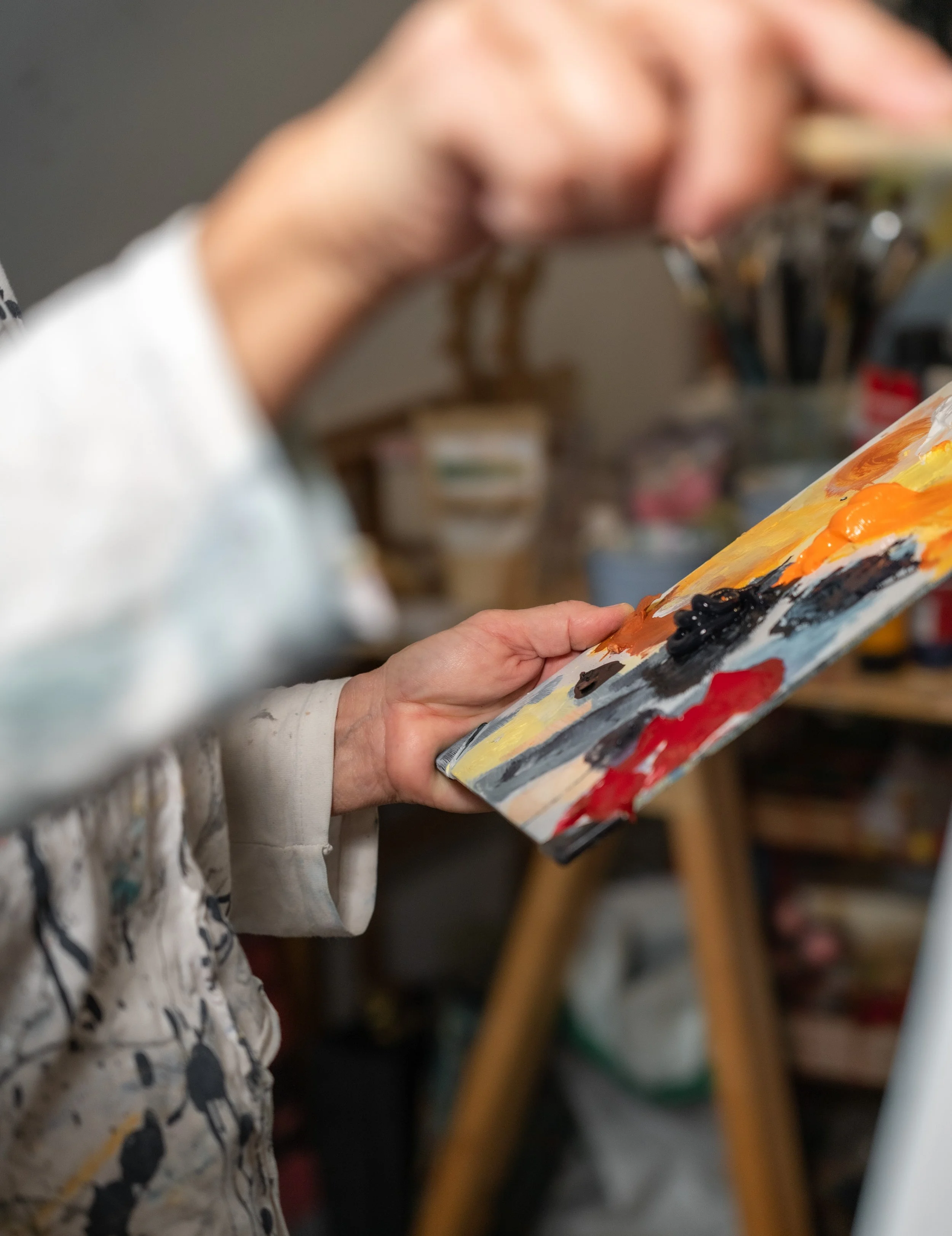 Person beim Malen auf einer Leinwand. In der Linken Hand hält sie eine Palette mit Farben in der rechten einen großen Pinsel.
