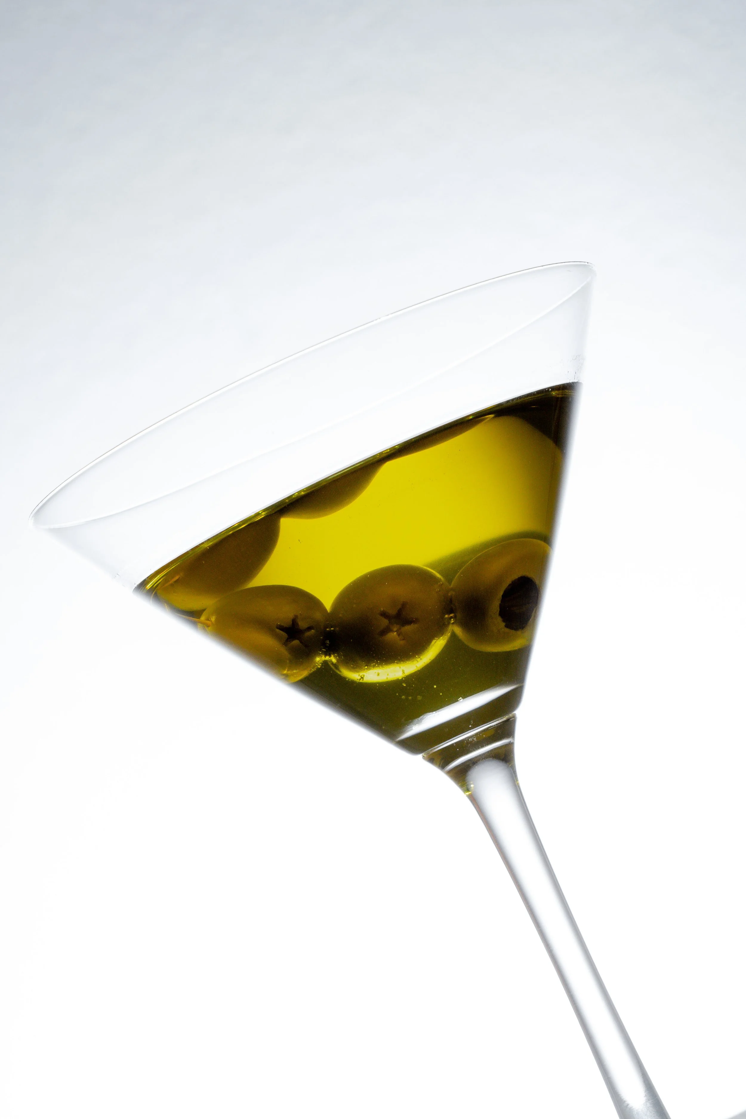 Weinglas mit grünen Oliven und schwarzen Oliven, gefüllt mit Wein, gegen weißen Hintergrund.