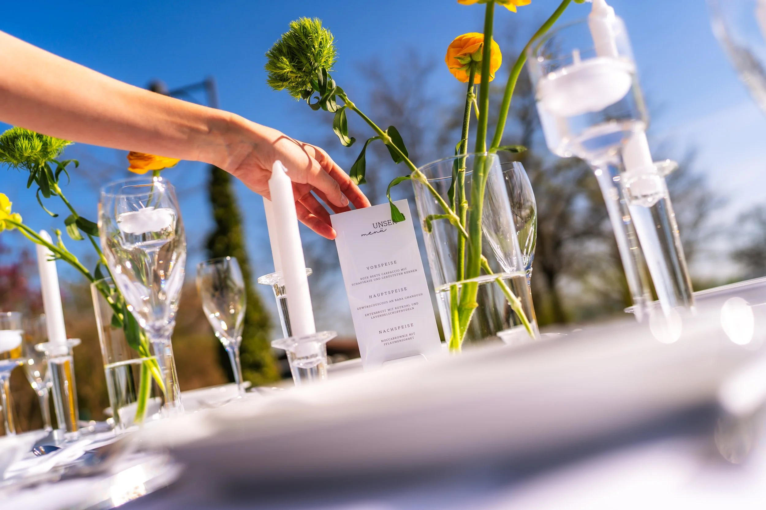 Blumenstrauß mit gelben und grünen Blumen in Gläsern auf einem Tisch im Freien bei blauem Himmel.