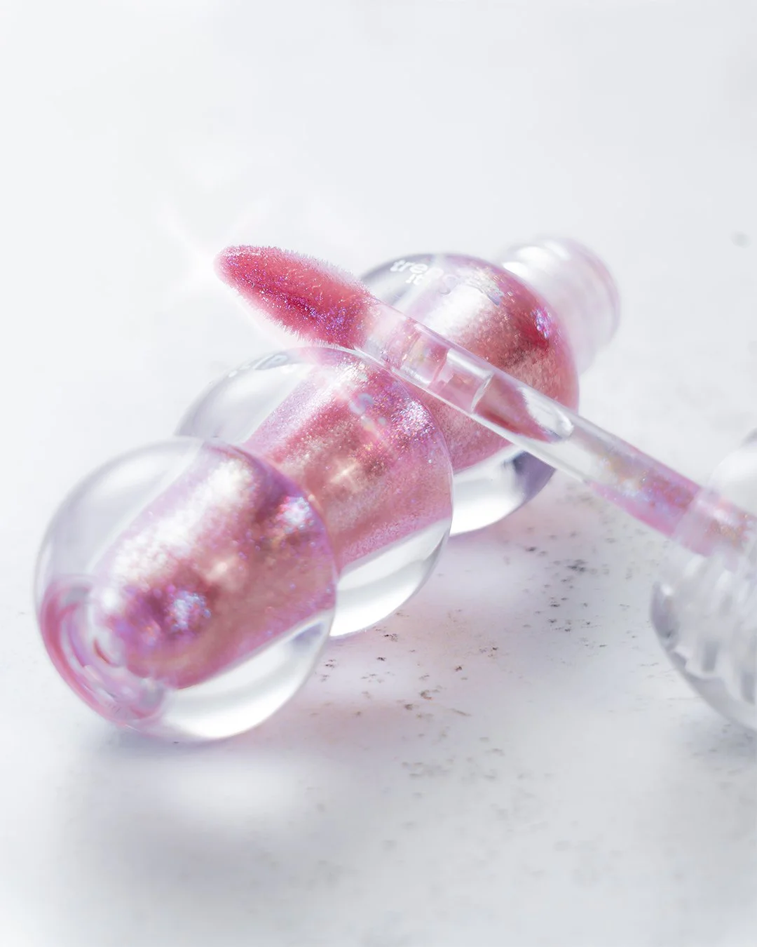 Ein offenes Lipgloss-Fläschchen mit pinkem Lipgloss auf einer weißen Oberfläche.