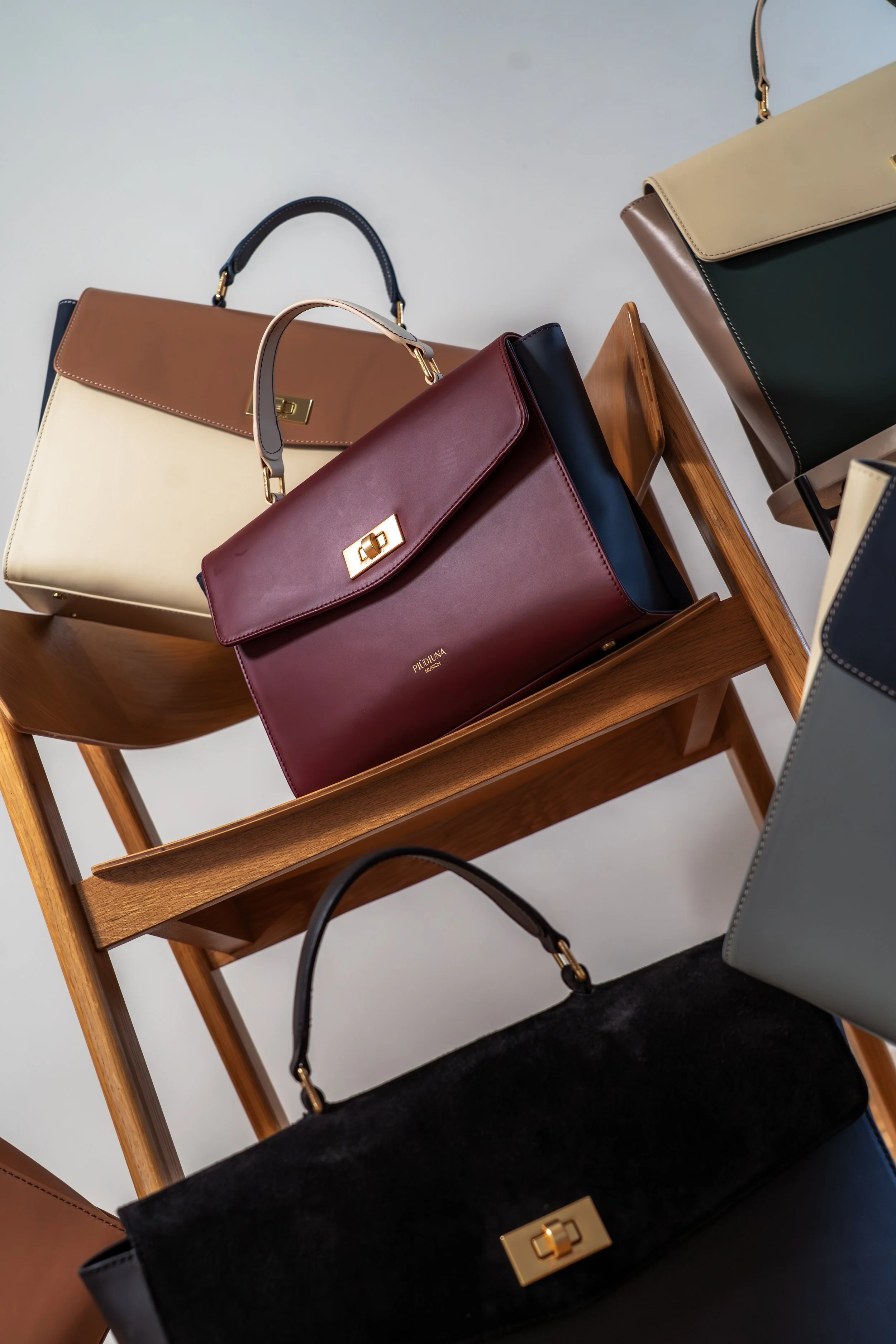 Verschiedene Handtaschen in verschiedenen Farben und Materialien stehen auf einem Holzstuhl.