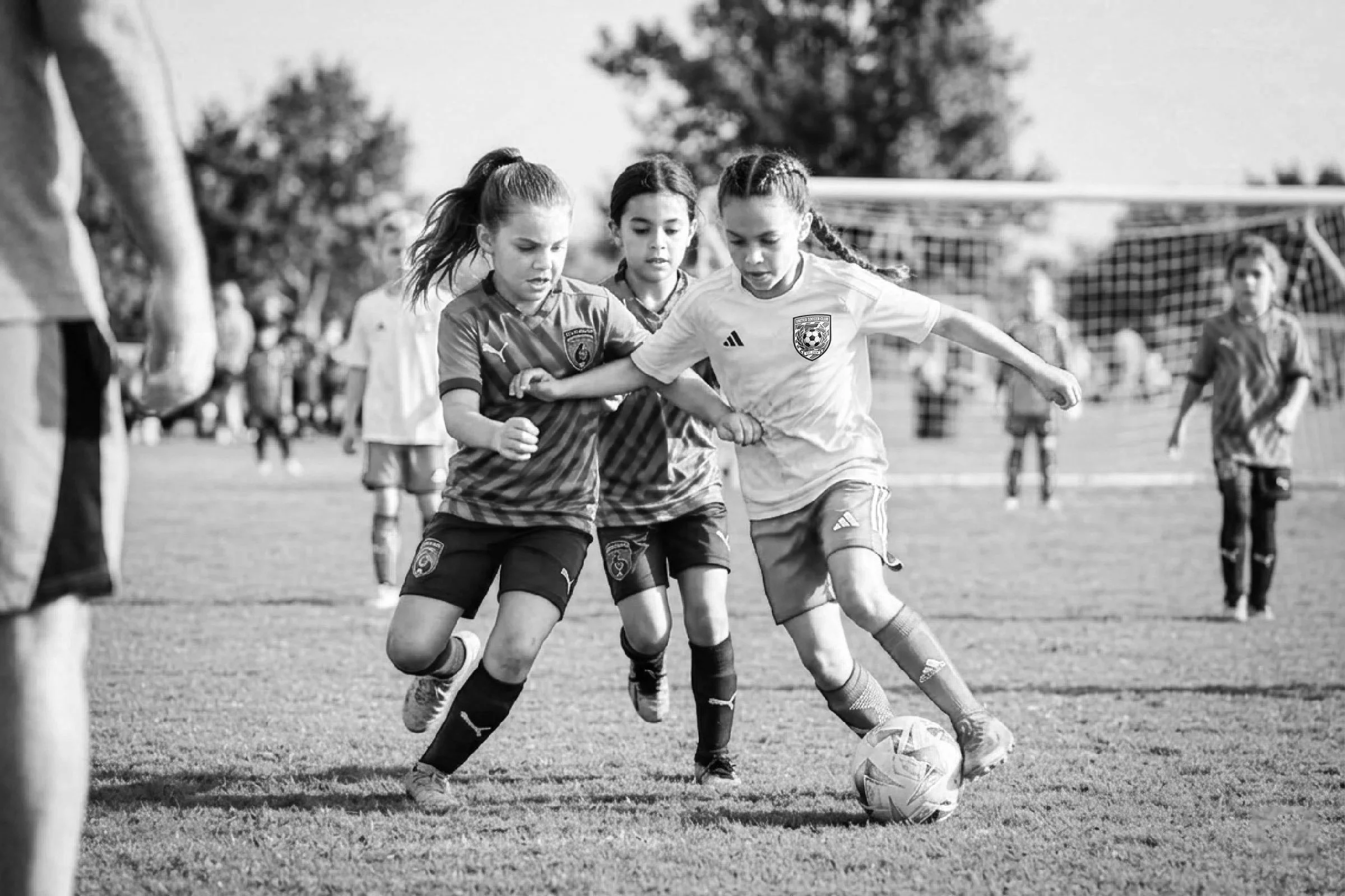 Children playing soccer on a field, with a focus on two girls battling for possession of the ball.