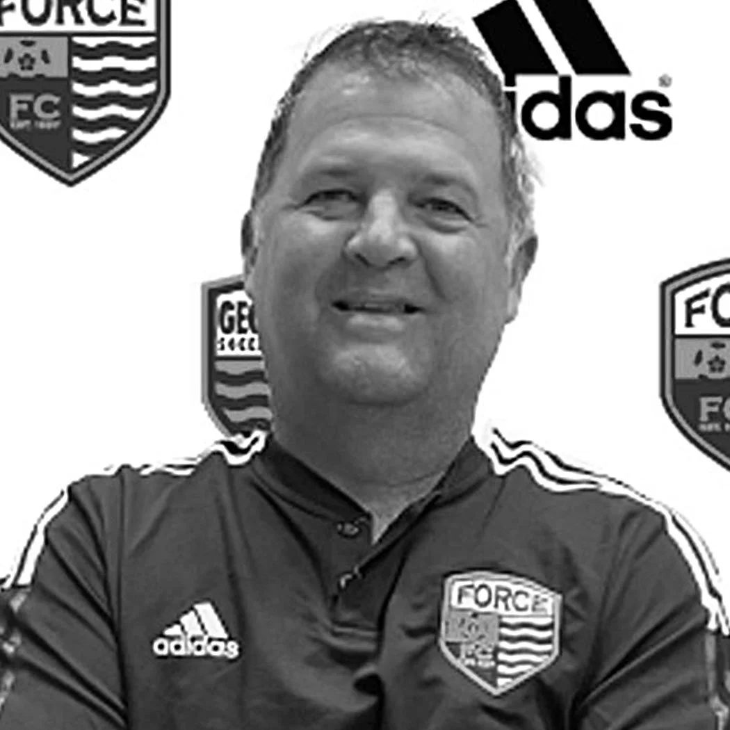Black and white photo of a smiling man wearing a sports jersey with the United States Forest Service badge, standing in front of a backdrop with the Forest Service shield, Adidas logo, and other official emblems.