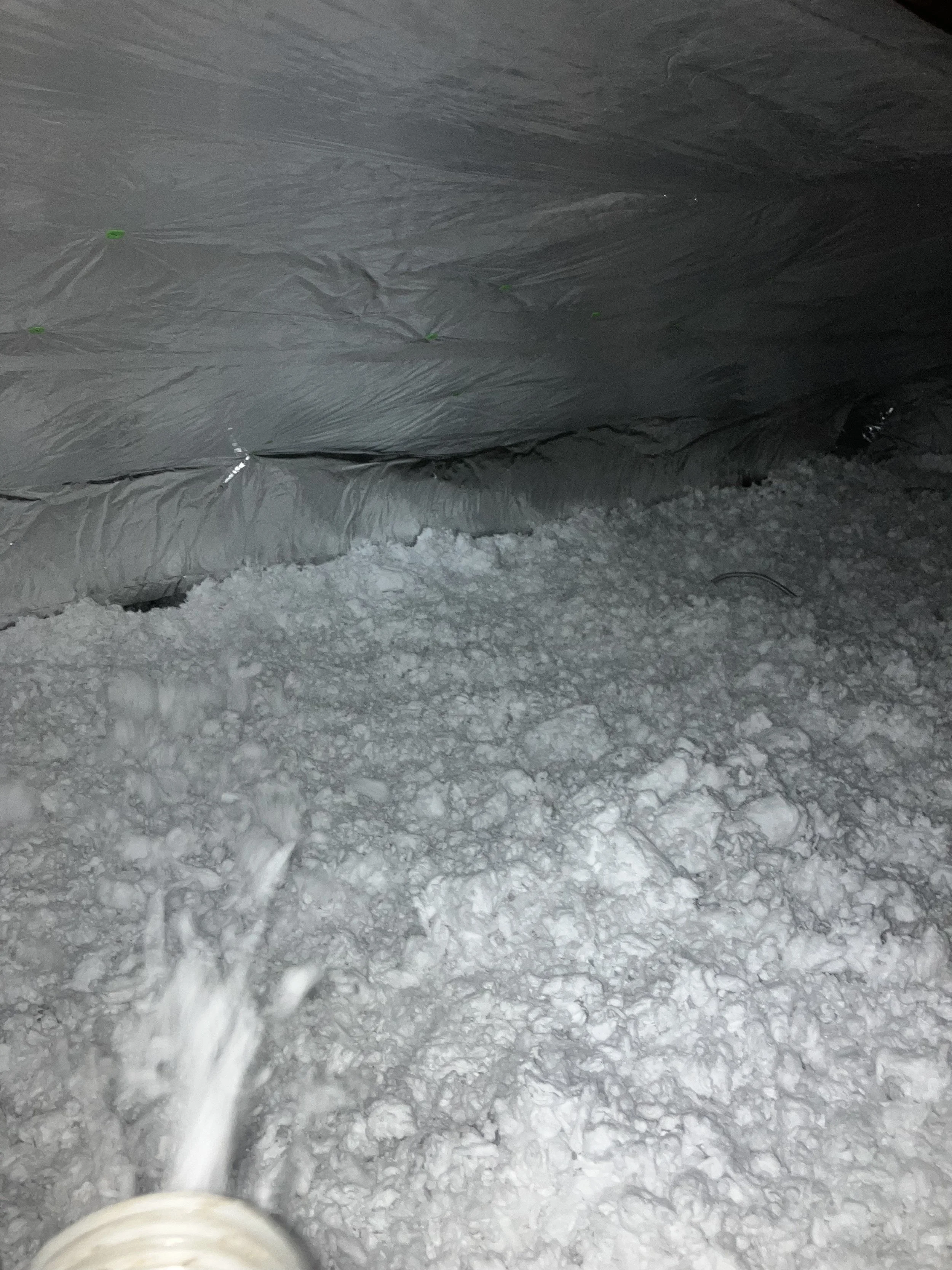 Snowy ground with footprints and a black object partially visible in the corner, covered by a tarp or plastic sheeting secured with green fasteners.
