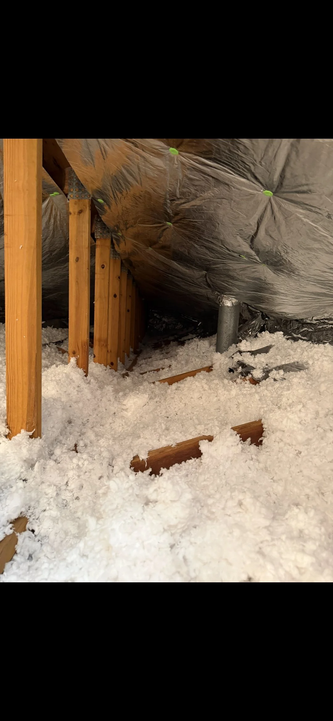Attic space with wooden beams, insulation, and silver vapor barrier, snow on the attic floor.