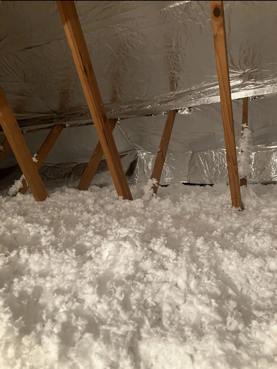 Attic with exposed wooden beams, insulation, and snow on the floor.