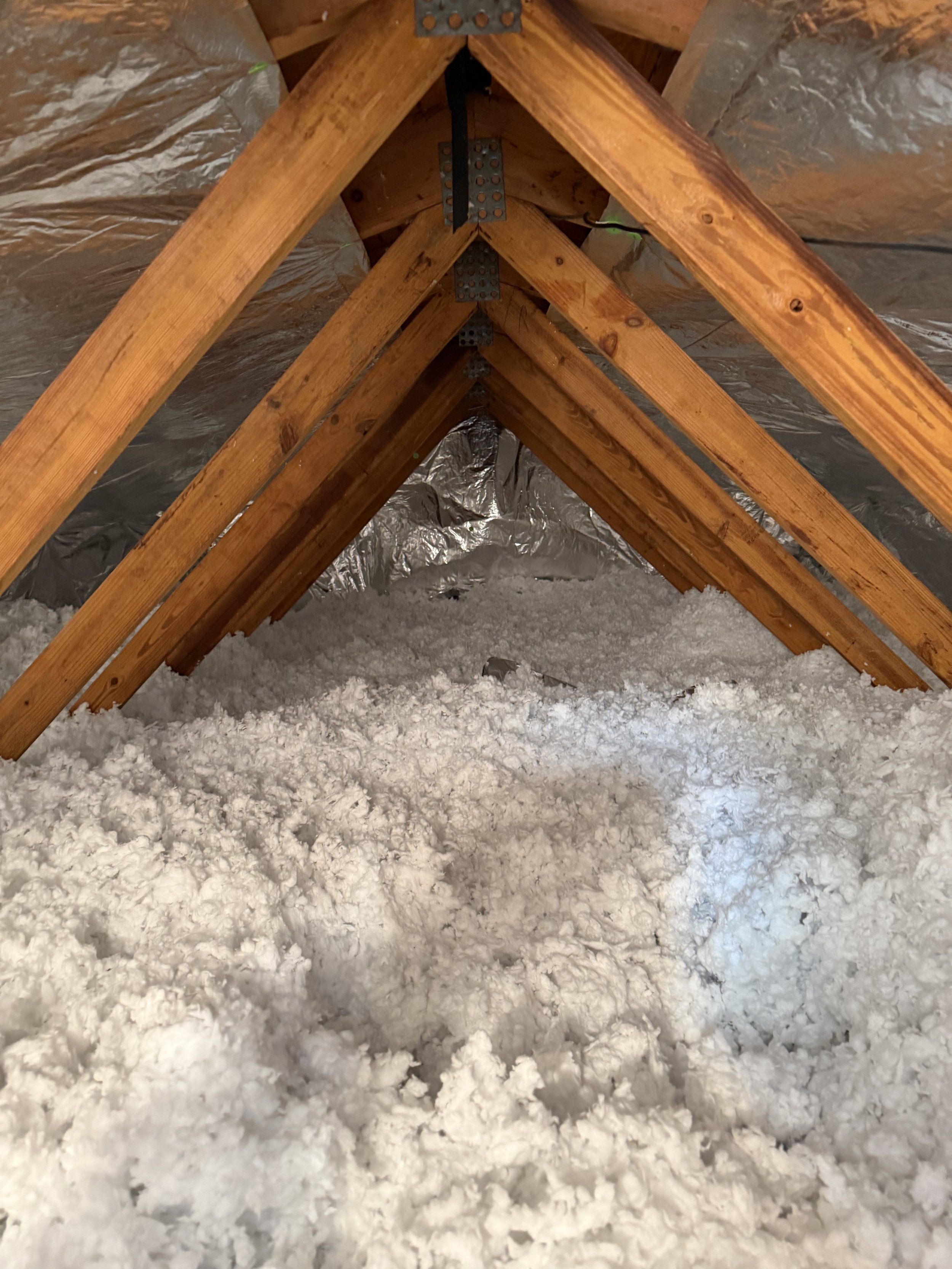 View of attic with wooden rafters, insulation foam on the floor, and reflective insulation material on the ceiling.