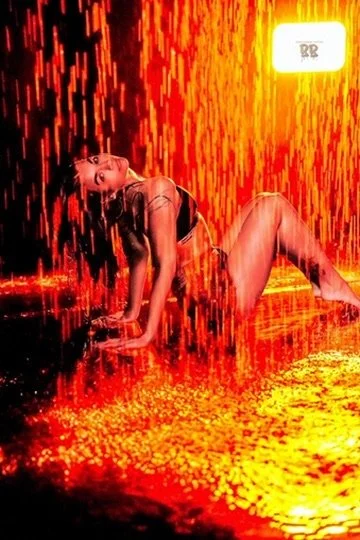 Photographer, for hire, Oceanside, Carlsbad, San Diego, Orange County, Fashion, Portraits, Moments, Lifestyle, Events, Branding.A woman in revealing clothing posing on the floor with red and orange lighting creating a fiery background and reflection.