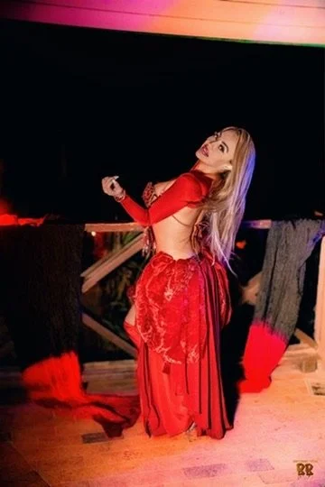 Photographer, for hire, Oceanside, Carlsbad, San Diego, Orange County, Fashion, Portraits, Moments, Lifestyle, Events, Branding.A woman with long blonde hair in a red outfit posing indoors at night, with a dark background and wooden floor.