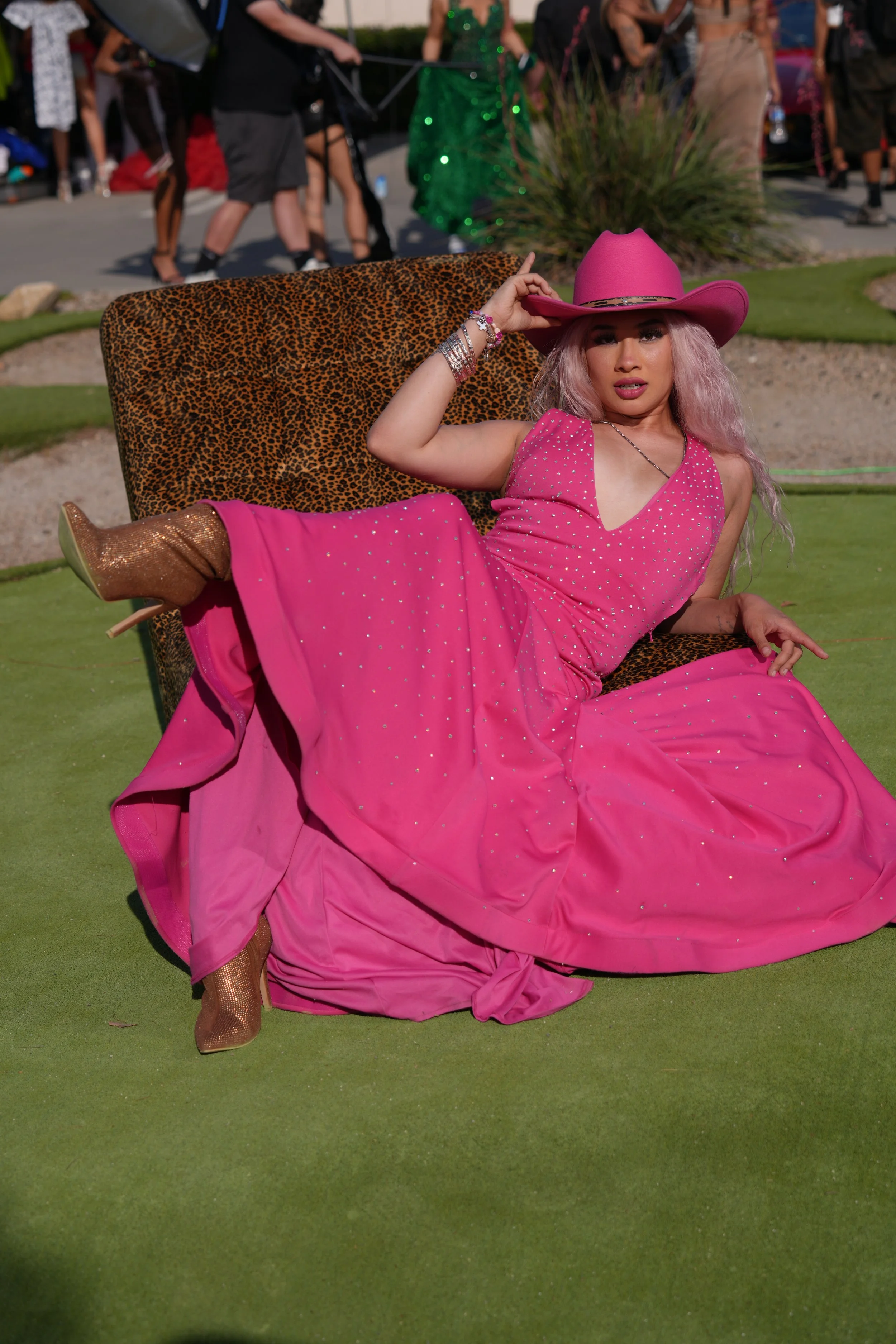 A woman with pink hair wearing a pink dress, cowboy hat, and cowboy boots, sitting on a leopard print chair outdoors at a gathering or event.Photographer, for hire, Oceanside, Carlsbad, San Diego, Orange County, Fashion, Portraits, Moments, Lifestyle