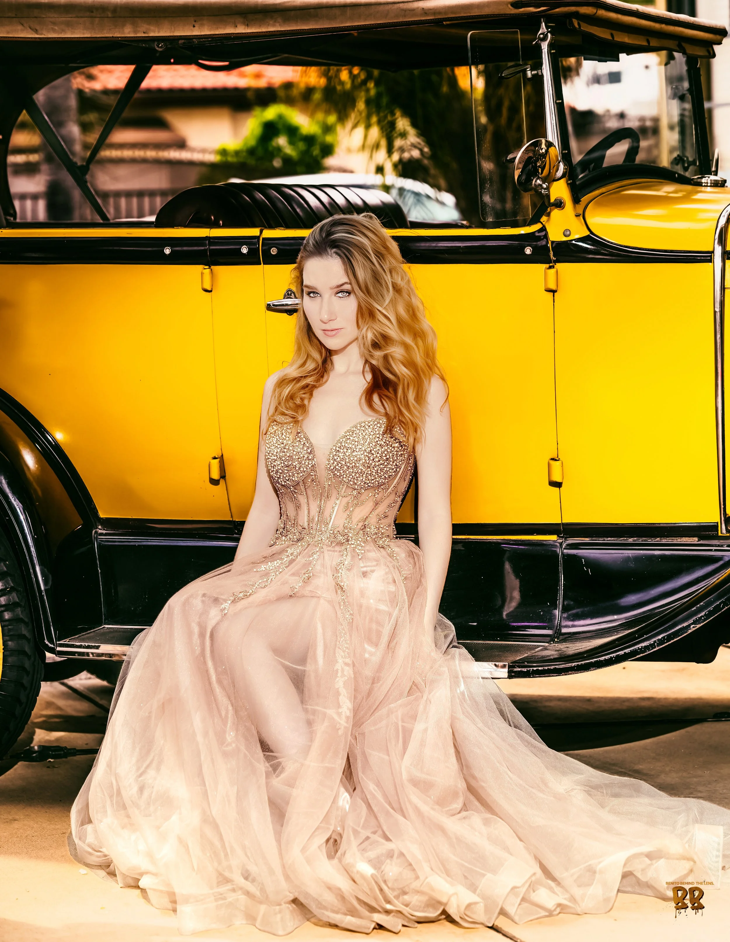 A woman with long, wavy blonde hair sits in front of a yellow vintage car wearing a glamorous, gold, strapless gown with a full, tulle skirt. Photographer, for hire, Oceanside, Carlsbad, San Diego, Orange County, Fashion, Portraits, Moments, Life.