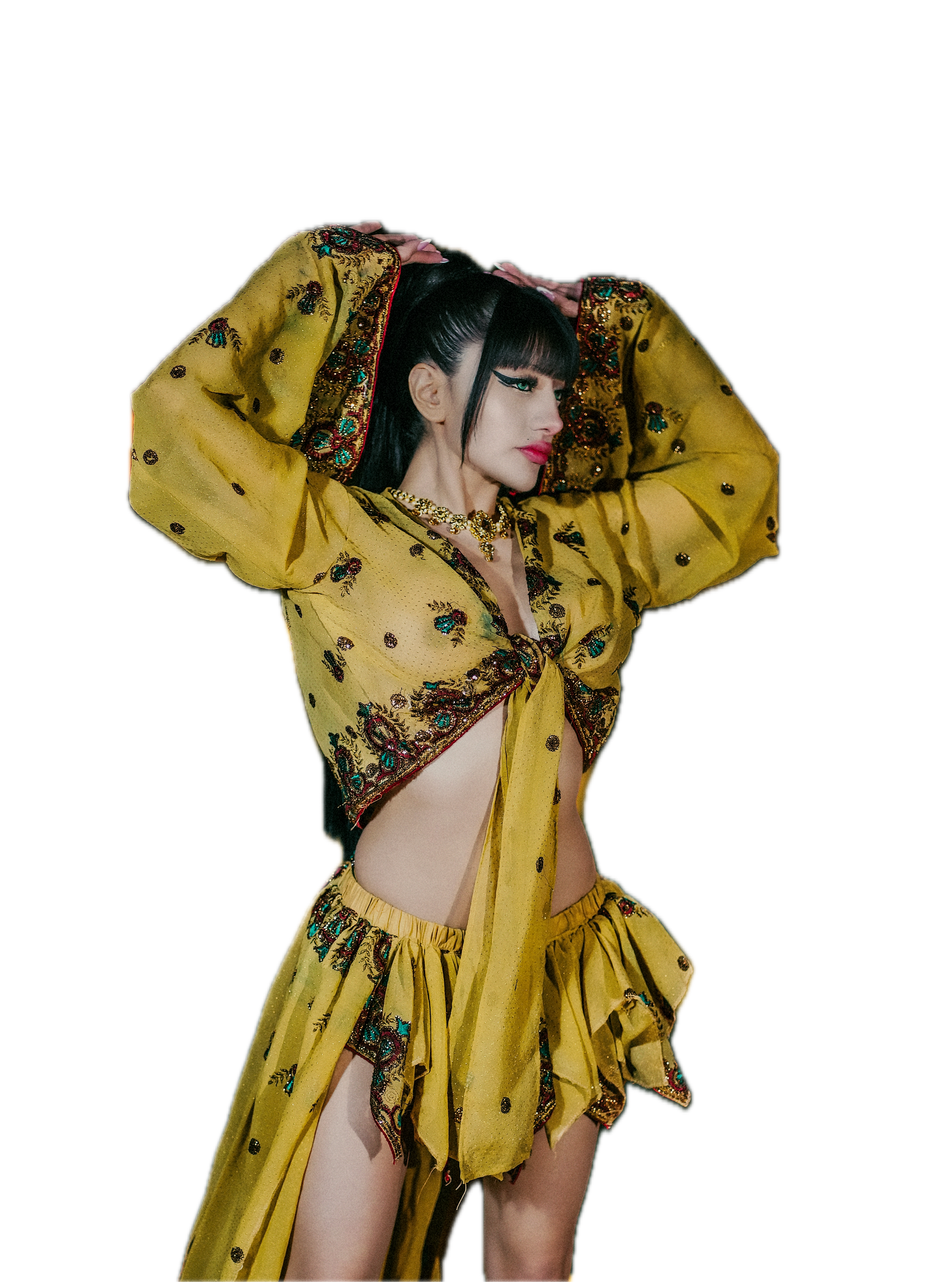 A woman posing in a yellow, embroidered outfit with jewelry and makeup, with her arms raised and hands on her head, against a black background.Photographer, for hire, Oceanside, Carlsbad, San Diego, Orange County, Fashion, Portraits, Moments, Lifesty