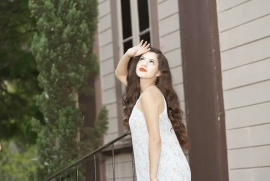 A woman with long brown hair and red lipstick standing outside near a house, looking up and shielding her eyes from the sun.Photographer, for hire, Oceanside, Carlsbad, San Diego, Orange County, Fashion, Portraits, Moments, Lifestyle, Events, Brandin