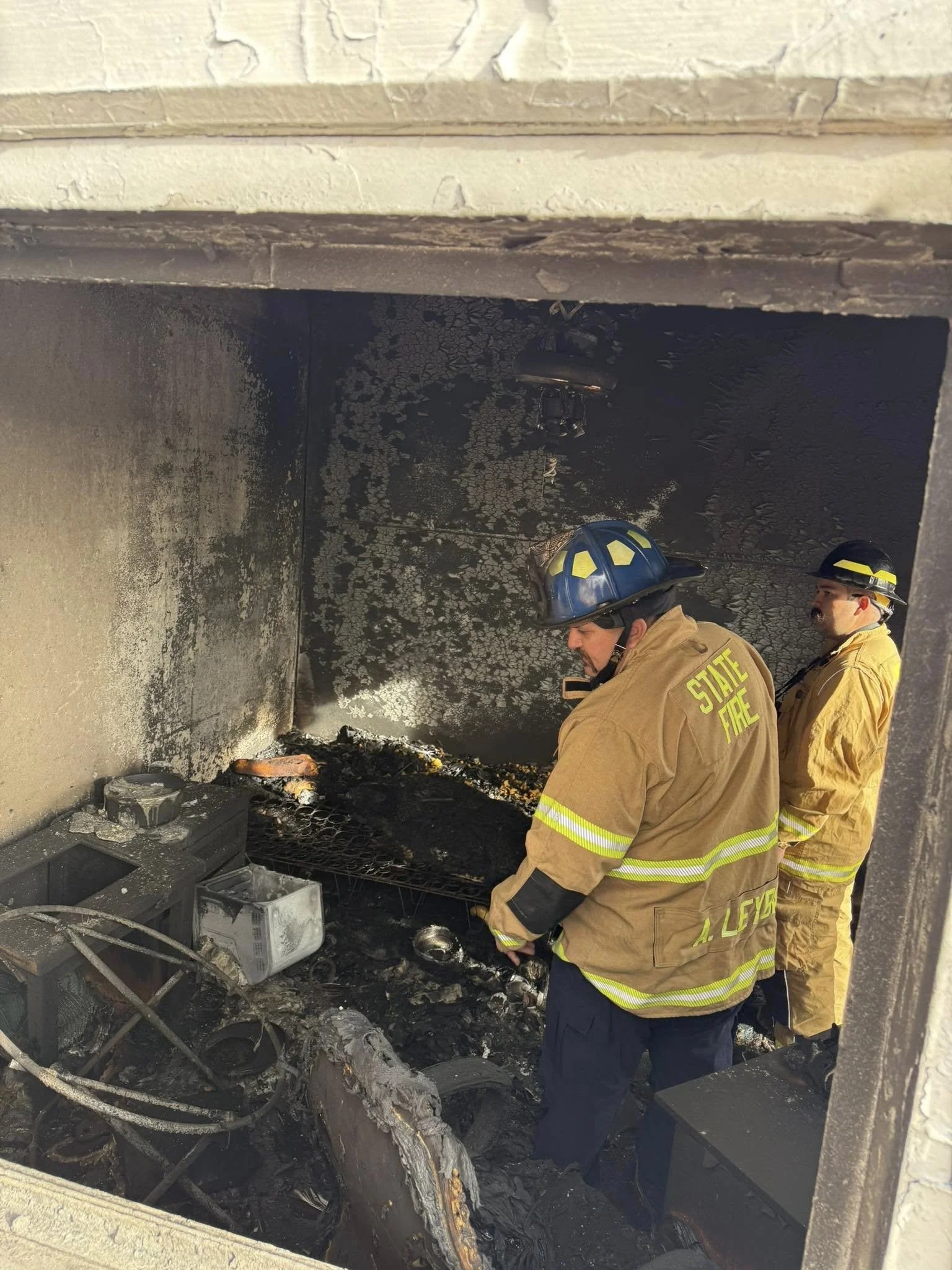Fire investigators at the scene of a fire in a building, inspecting the charred interior and debris, with visible fire damage and burnt equipment.