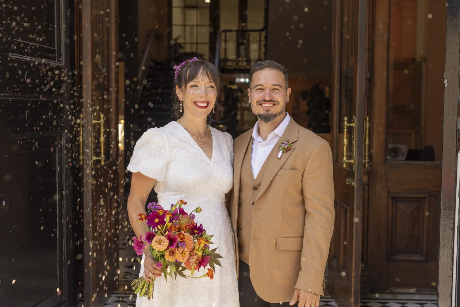 A couple just married, standing on the steps of the registry office with confetti in the air.