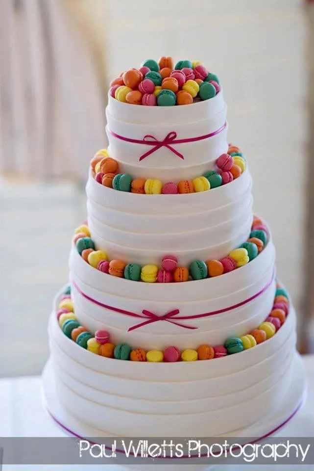 Multi-tiered white cake decorated with colorful round candies and pink ribbon accents.