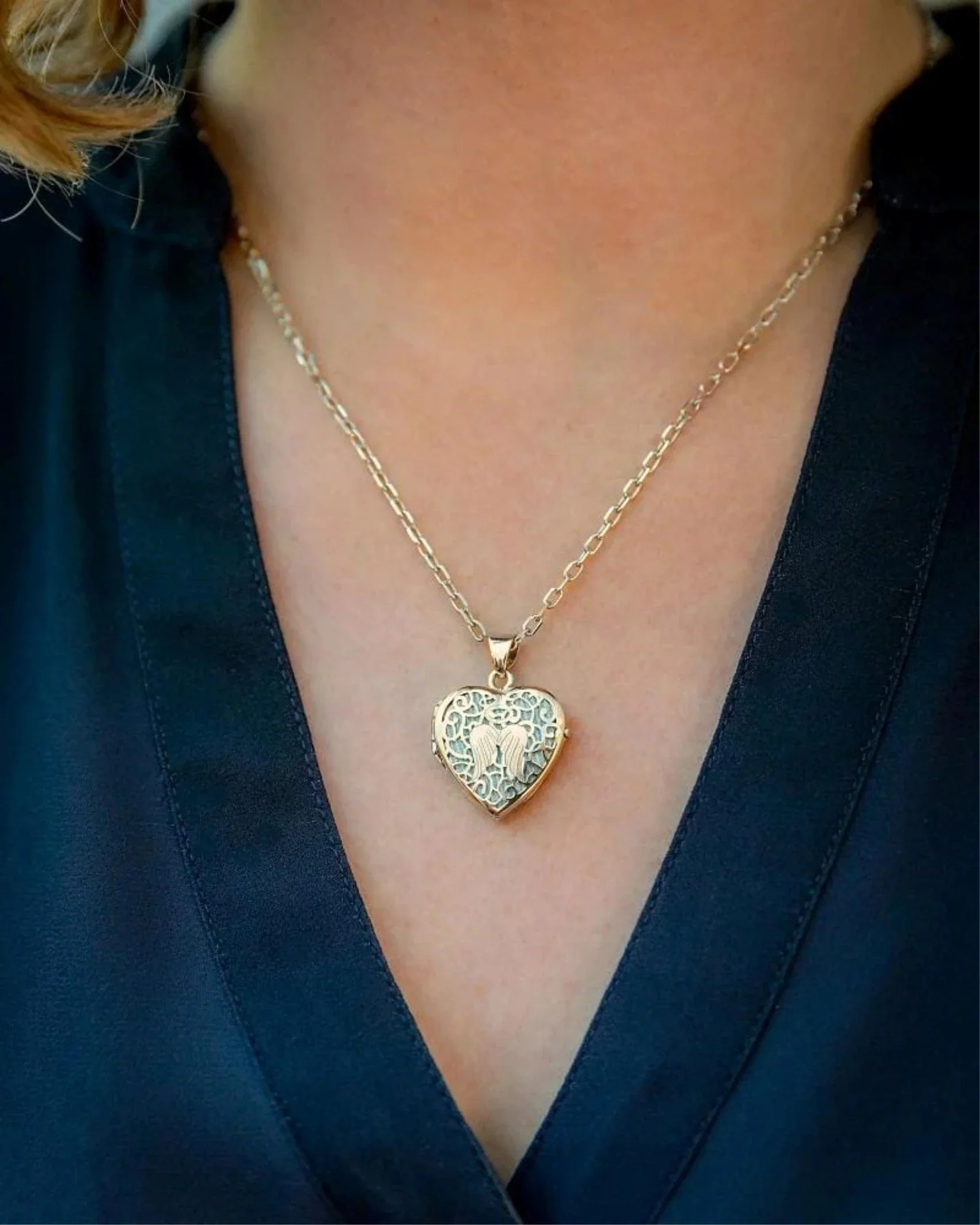 Close-up of a woman wearing a gold necklace with a heart-shaped pendant featuring an angel design, with part of her black clothing visible.