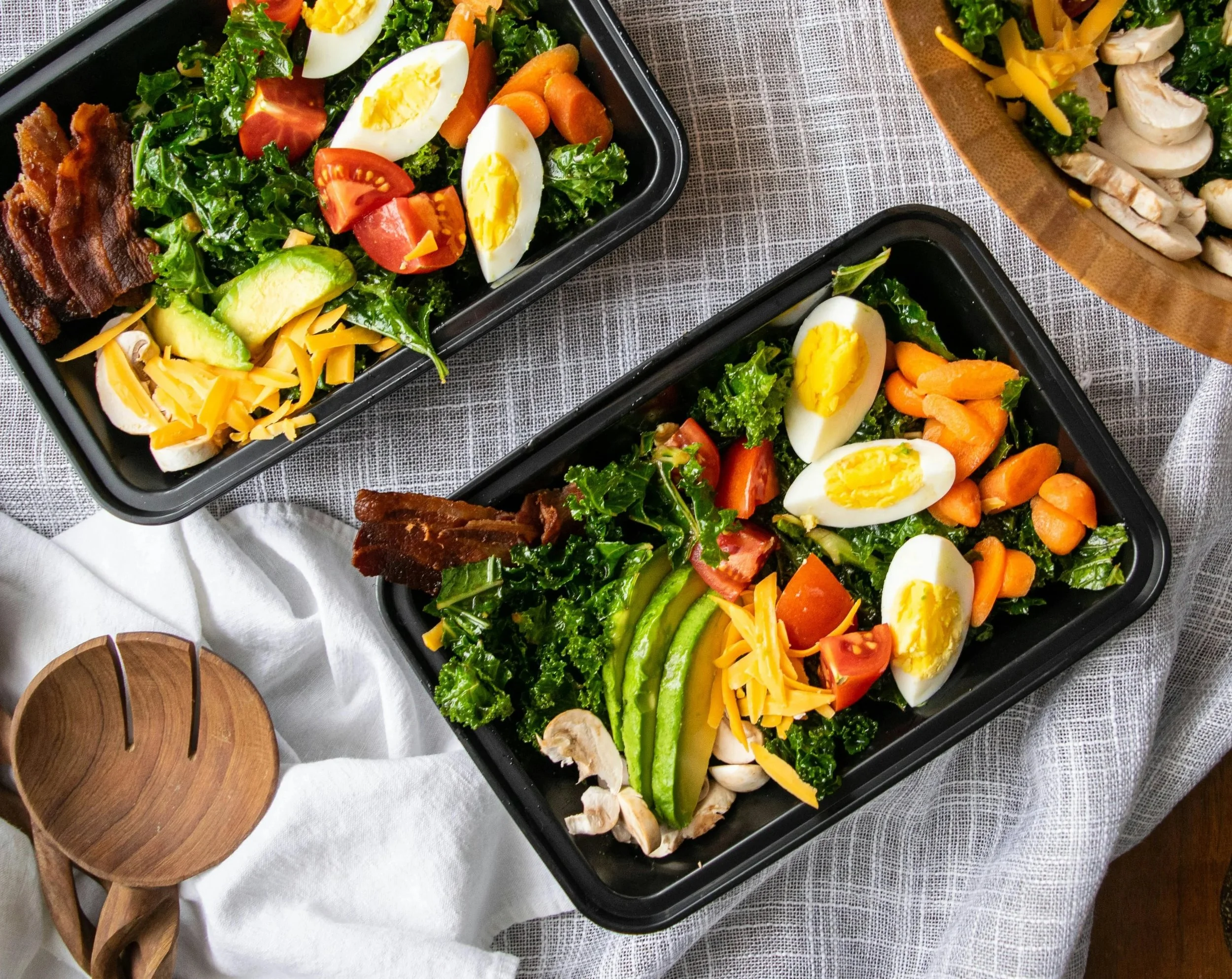 Lunch containers contain eggs, vegetables, bacon and mushrooms, on a bed of kale. Photo credit: Leanna Myers on Unsplash