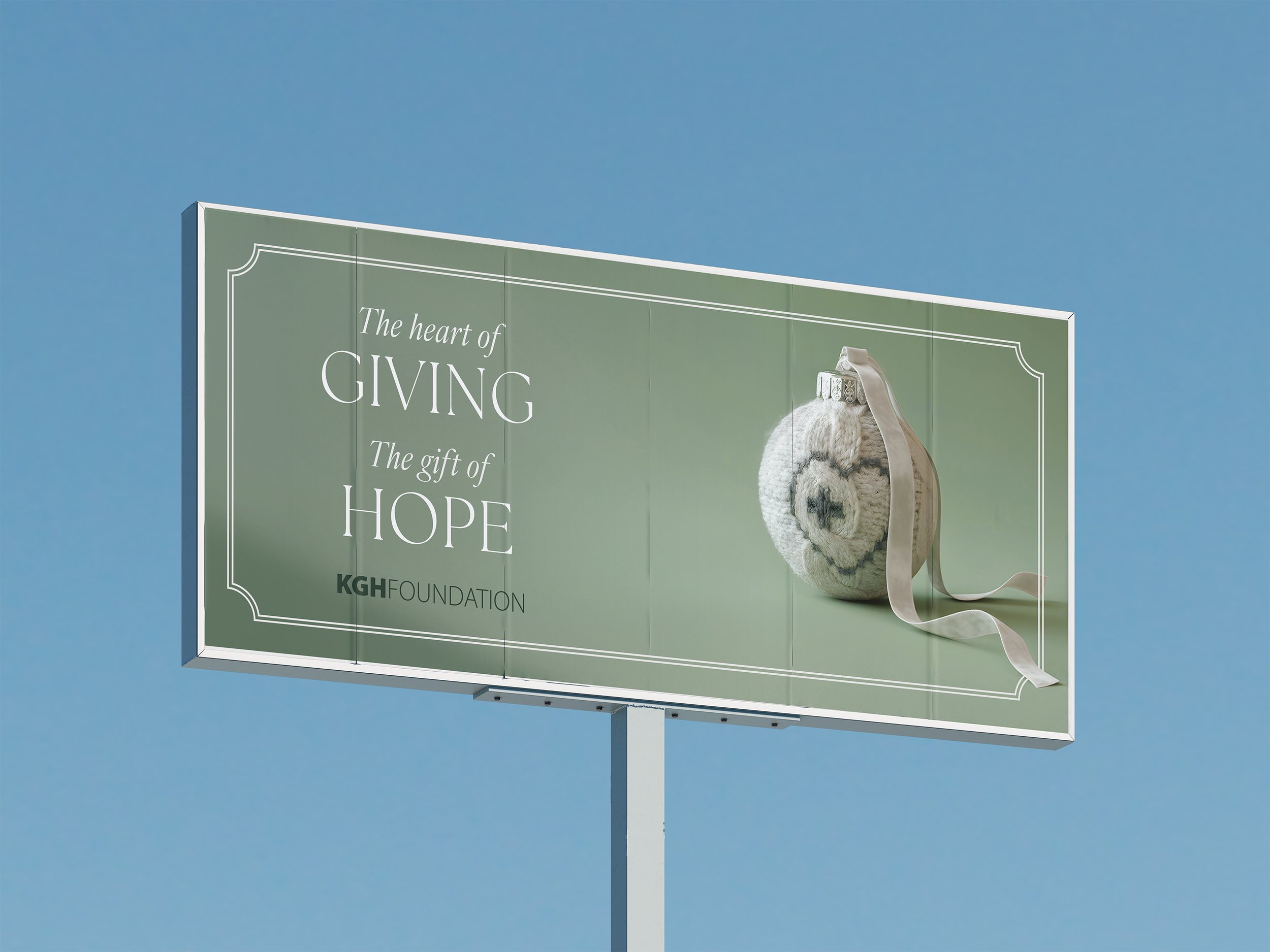 Billboard with an image of a heart-shaped rock wrapped with a ribbon, against a clear blue sky, with text about hope and giving from the KGH Foundation.