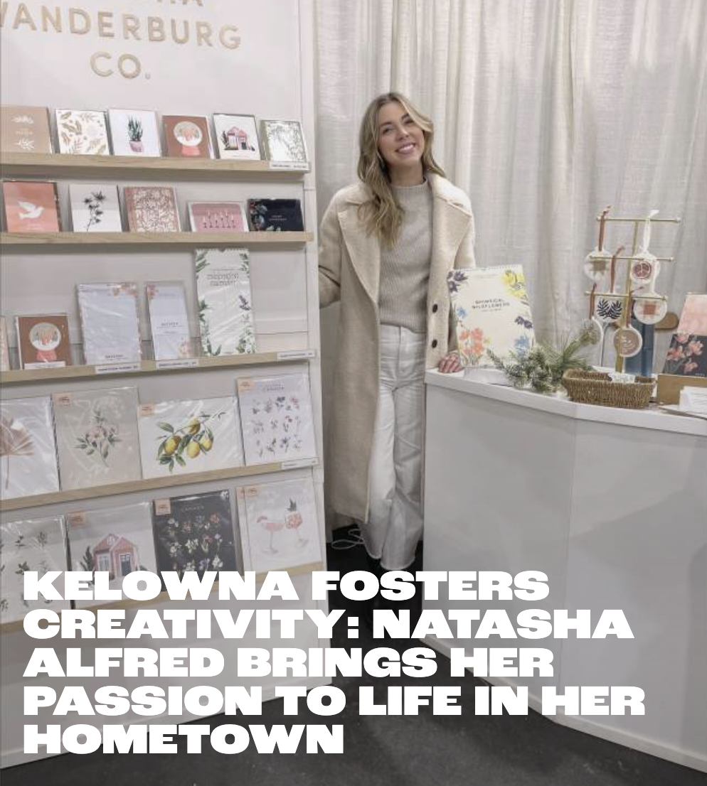 A woman in a beige coat and white pants standing inside a store with shelves displaying greeting cards with floral and nature designs. There are decorations on the table next to her and a sign that reads 'Sundries & Gift Wrap'.