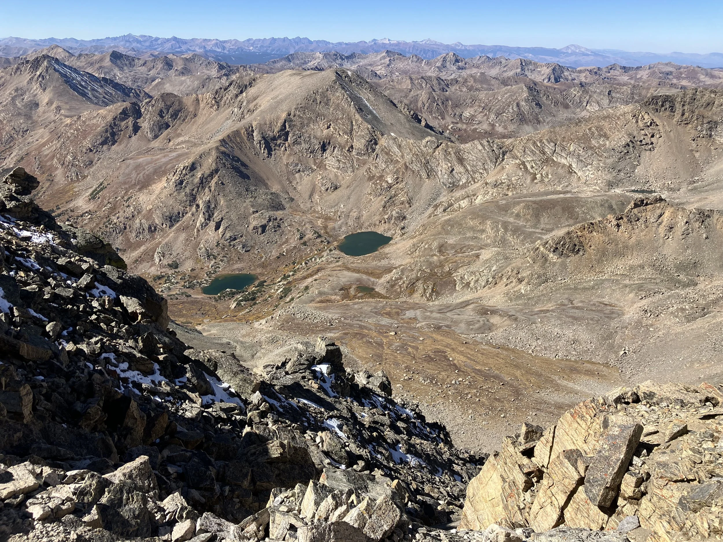 Mountains with rocky terrain, small lakes, and sparse vegetation beneath a clear sky.