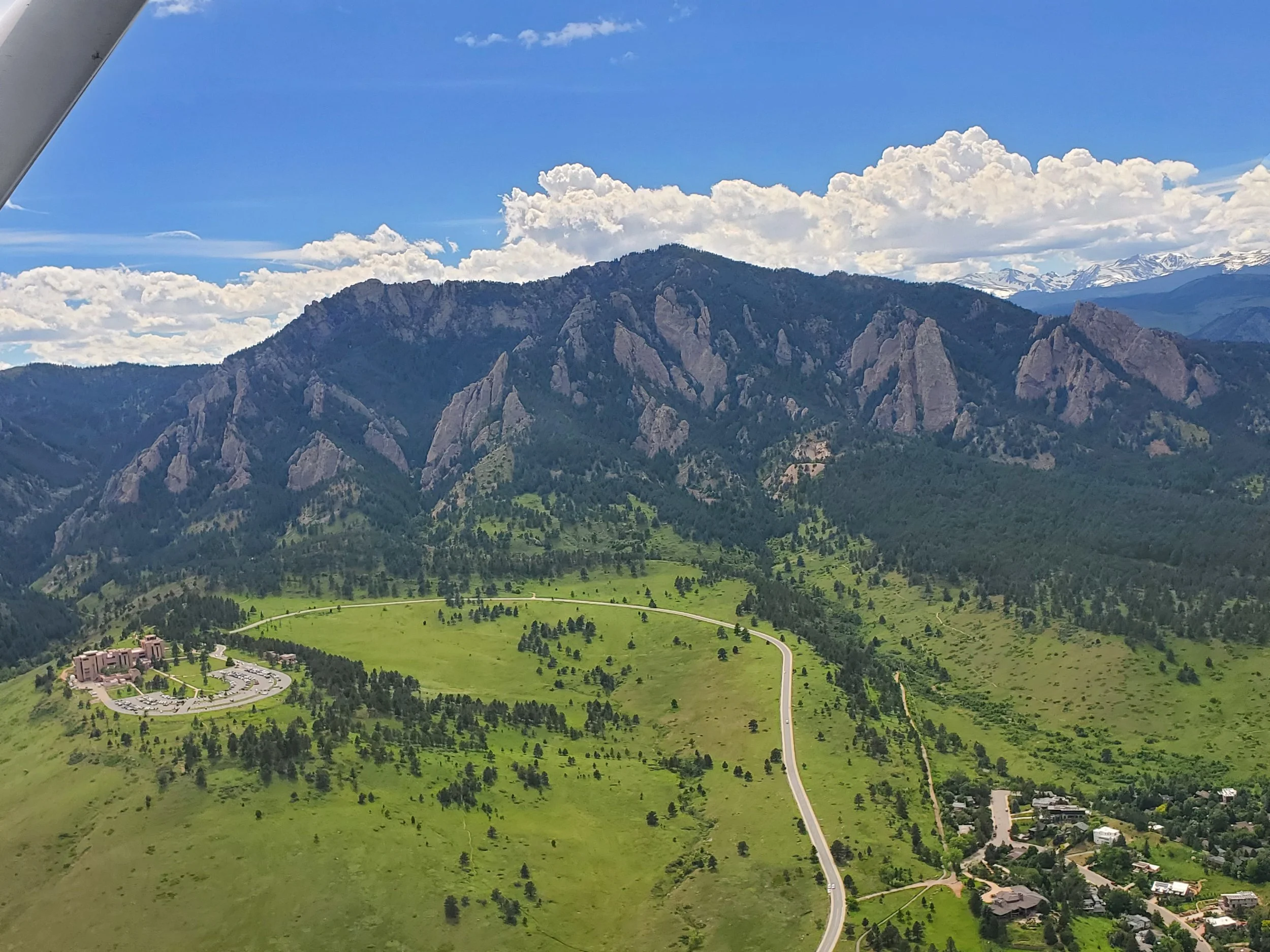 A mountainous landscape with rugged peaks, green valley, and a small residential area at the base of the mountains.
