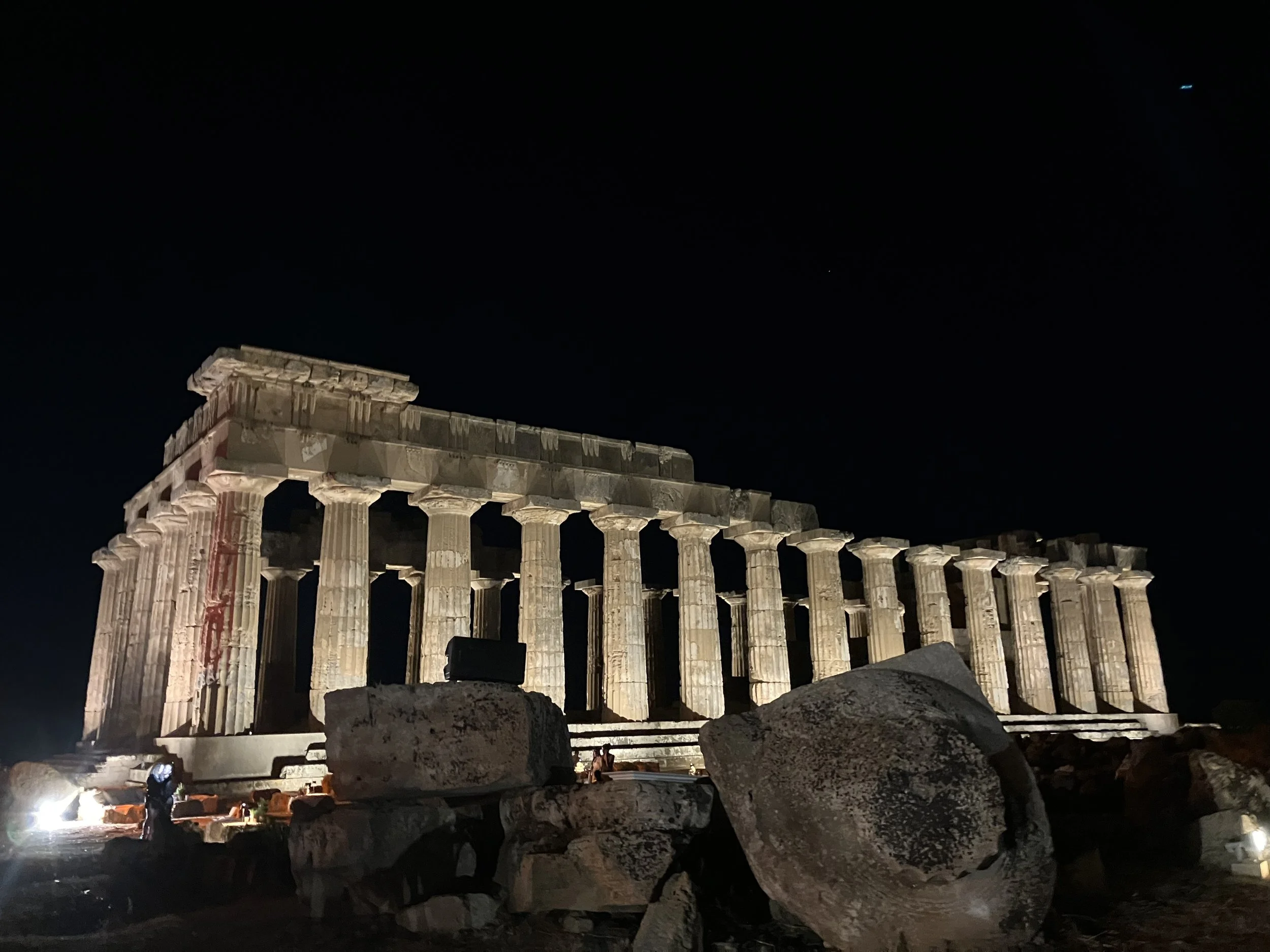 Ancient Greek ruins of a temple at night, illuminated by artificial lights, with the dark night sky above.