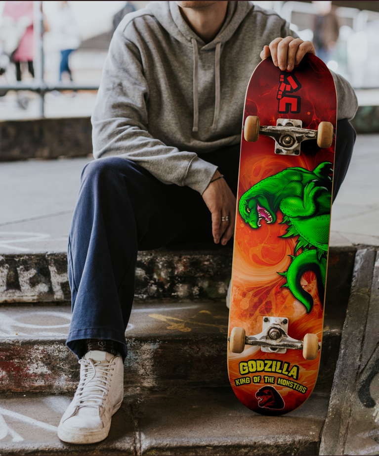 Person sitting on concrete stairs holding a skateboard with a Godzilla design.