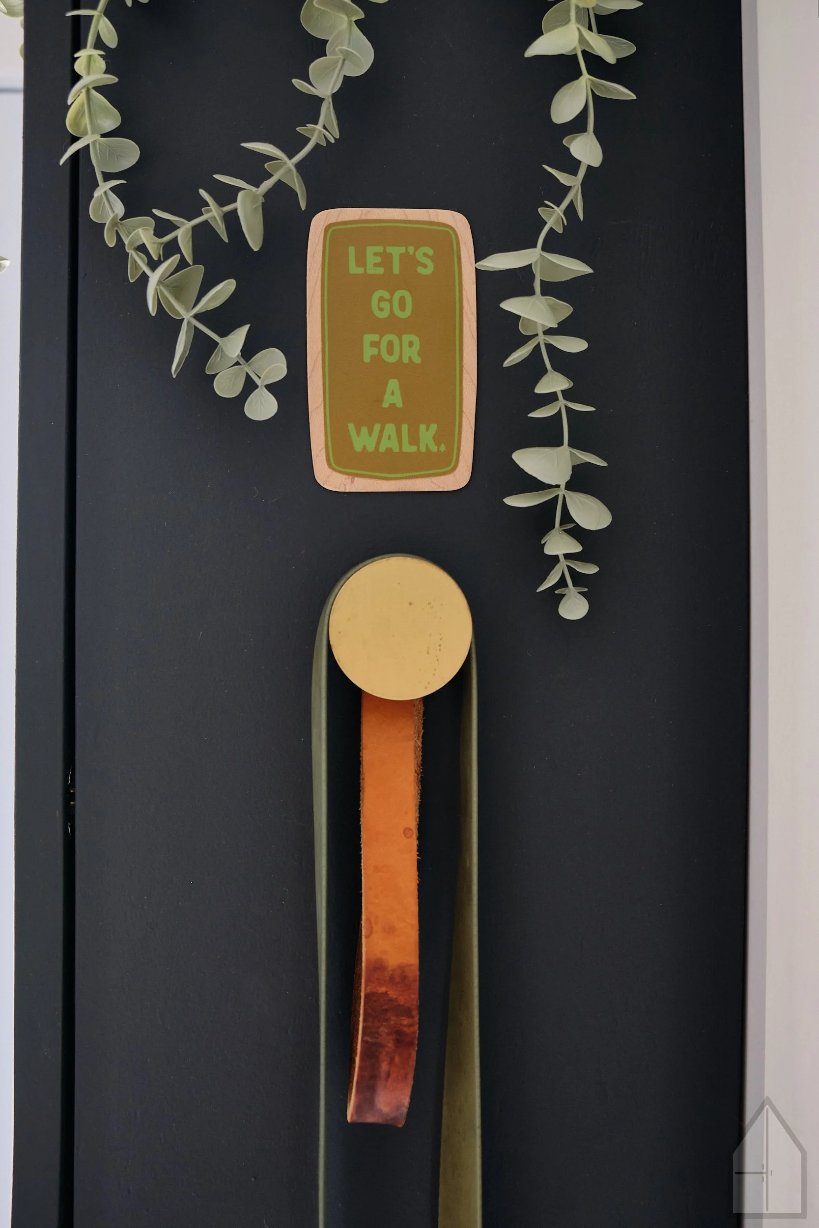 Close-up of a wall hanging with a sign that says "Let's go for a walk," someone’s framed photo from behind and to the side, with a string of faux green leaves hanging above.