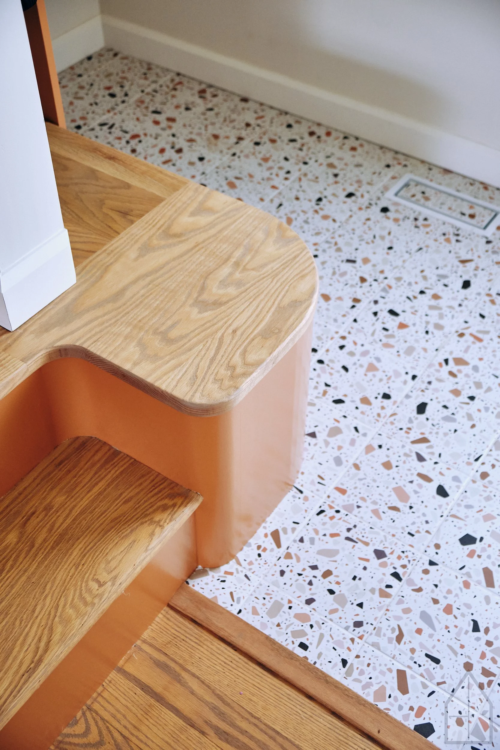 Close-up of wooden staircase next to terrazzo flooring and wall with baseboard.