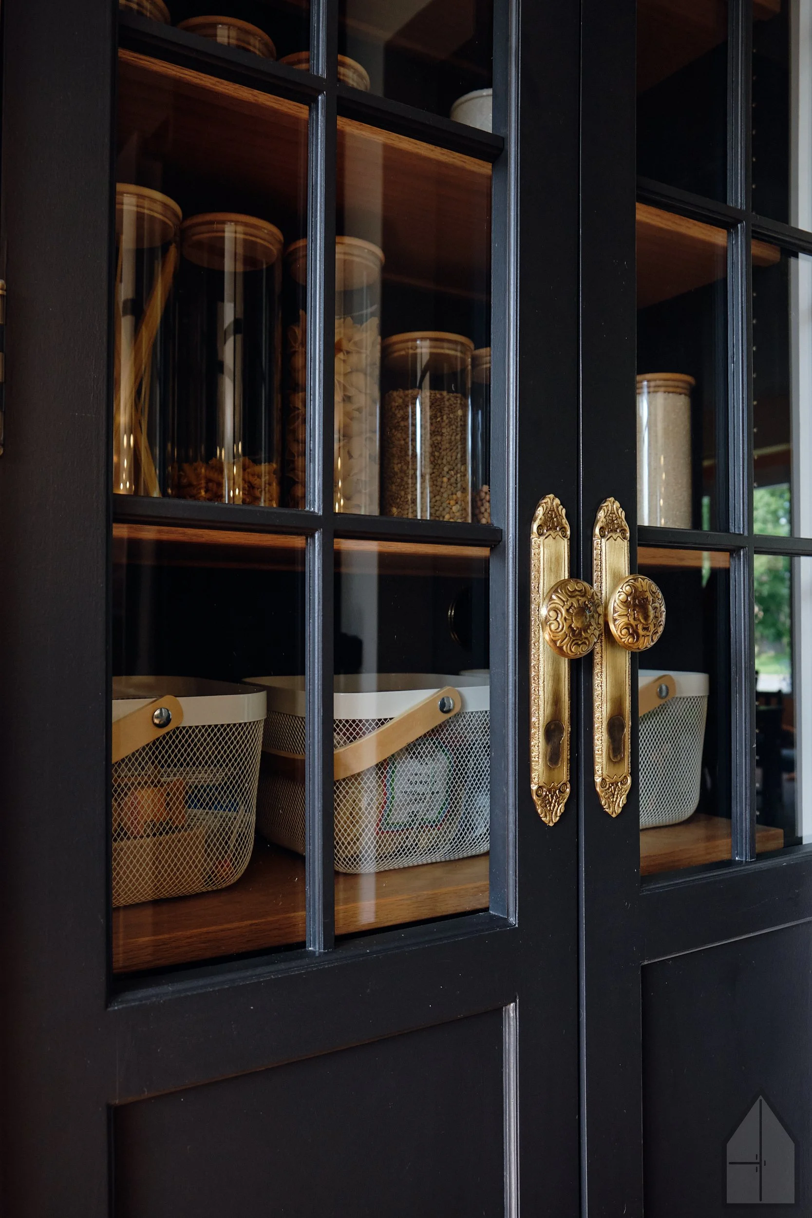 Kitchen cabinet with glass doors containing storage jars and baskets