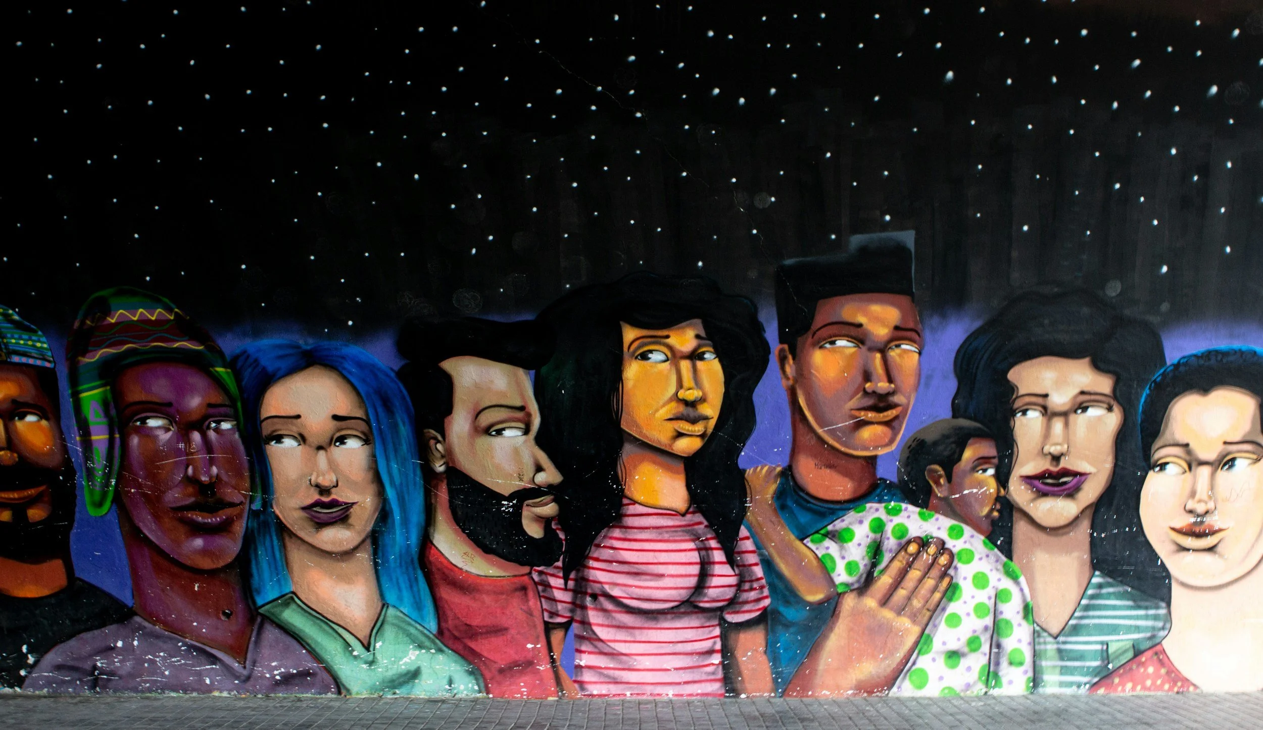 Colorful mural of diverse women's faces with different hairstyles and expressions against a starry night sky background.