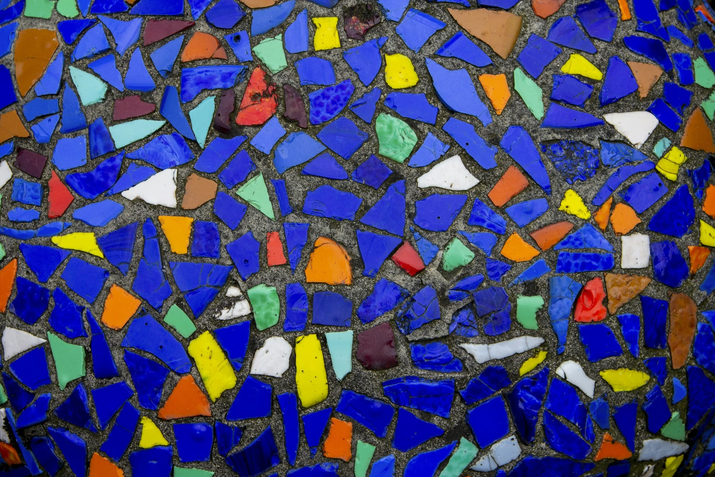 Close-up of a colorful mosaic made of broken ceramic tiles and glass pieces embedded in concrete.
