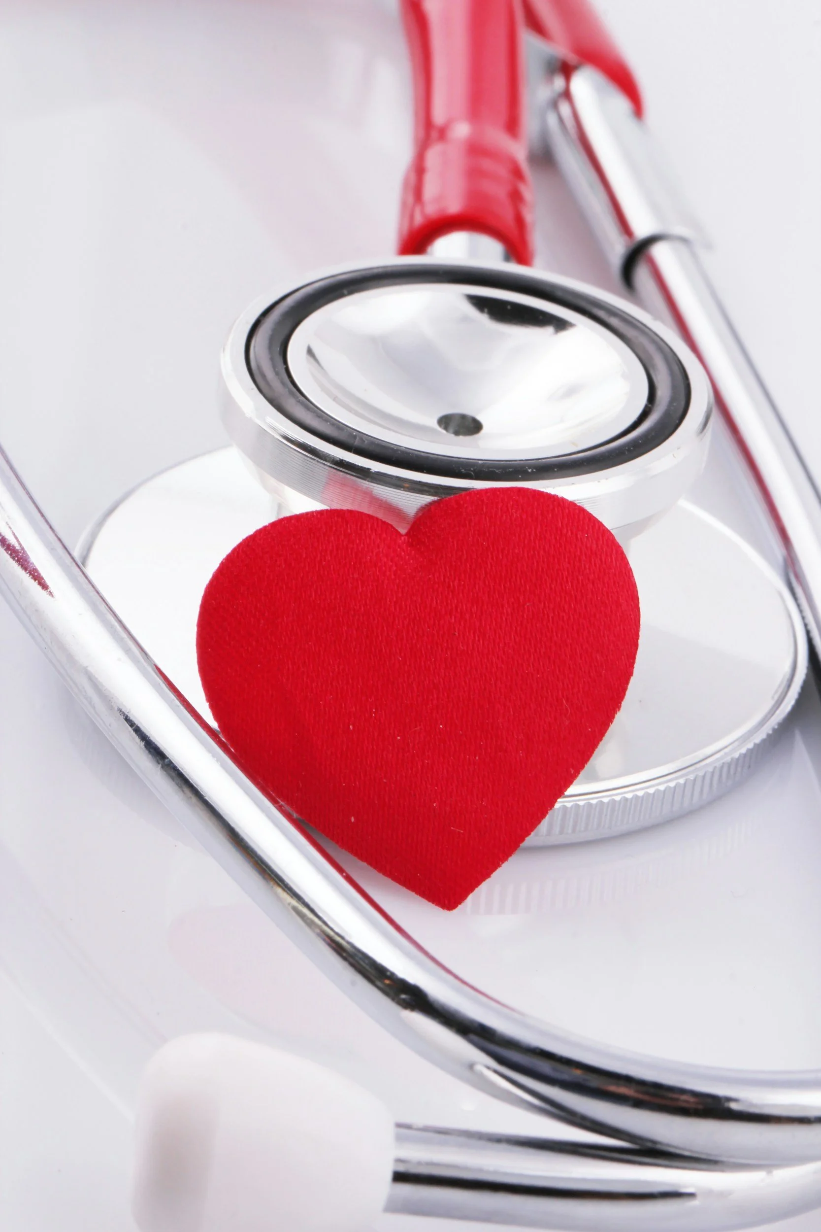 A silver stethoscope resting on a red felt heart with a white background.