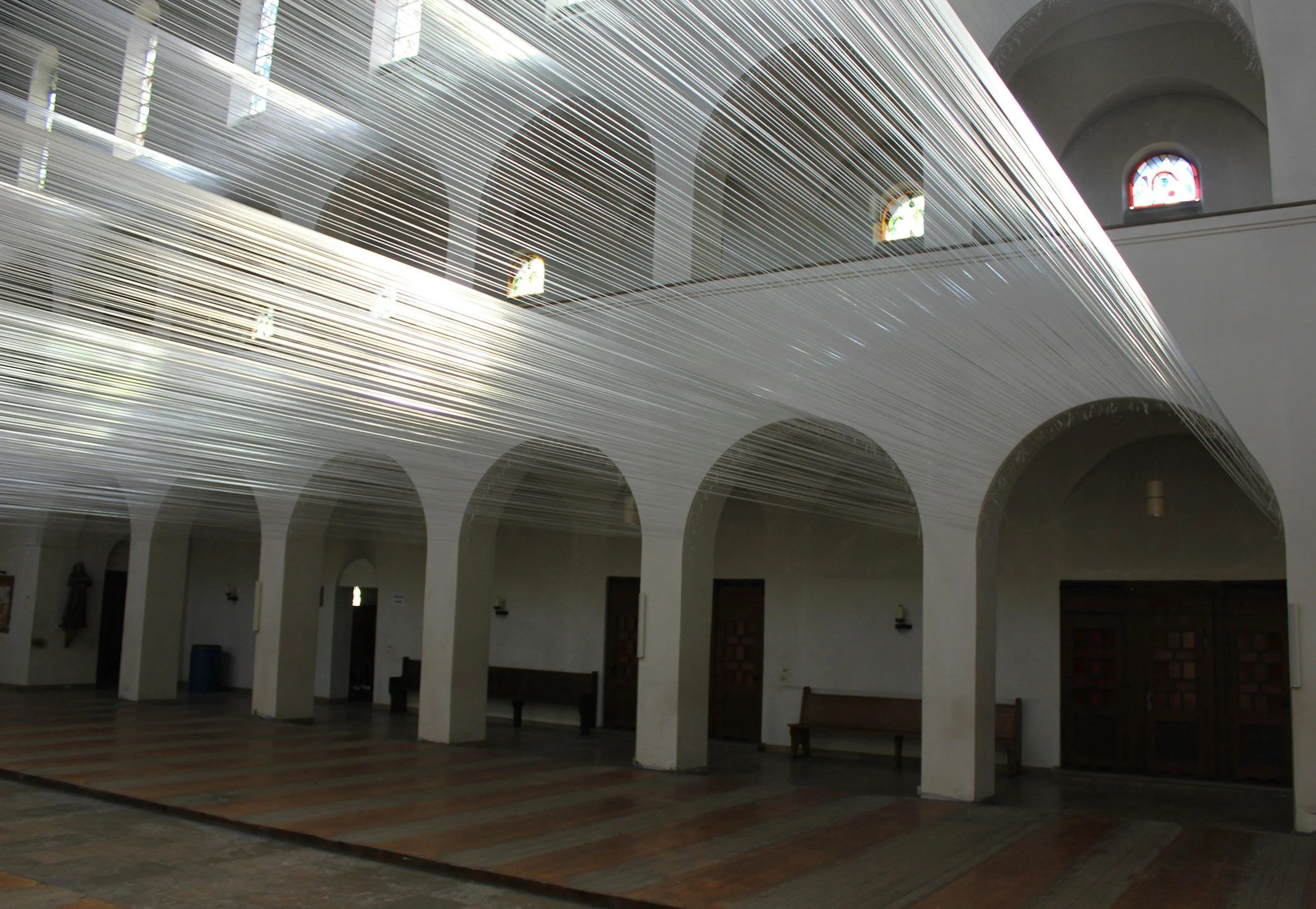 Interior view of a church with white arches, stained glass windows, wooden benches, and a high ceiling. The image features a streaked light effect across the space.