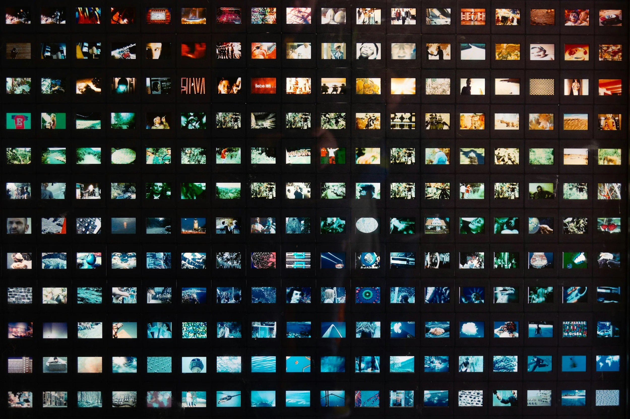 A wall with multiple small digital screens displaying vibrant and varied images, including people, landscapes, and abstract visuals.