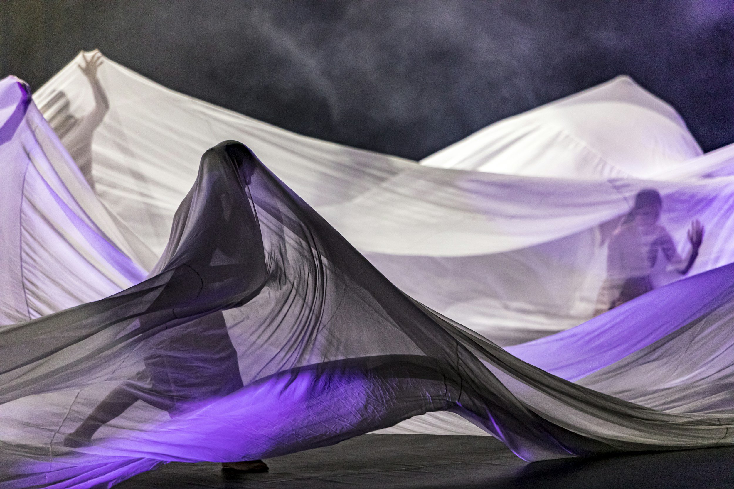 People behind translucent fabric with purple lighting, creating a surreal, abstract scene.