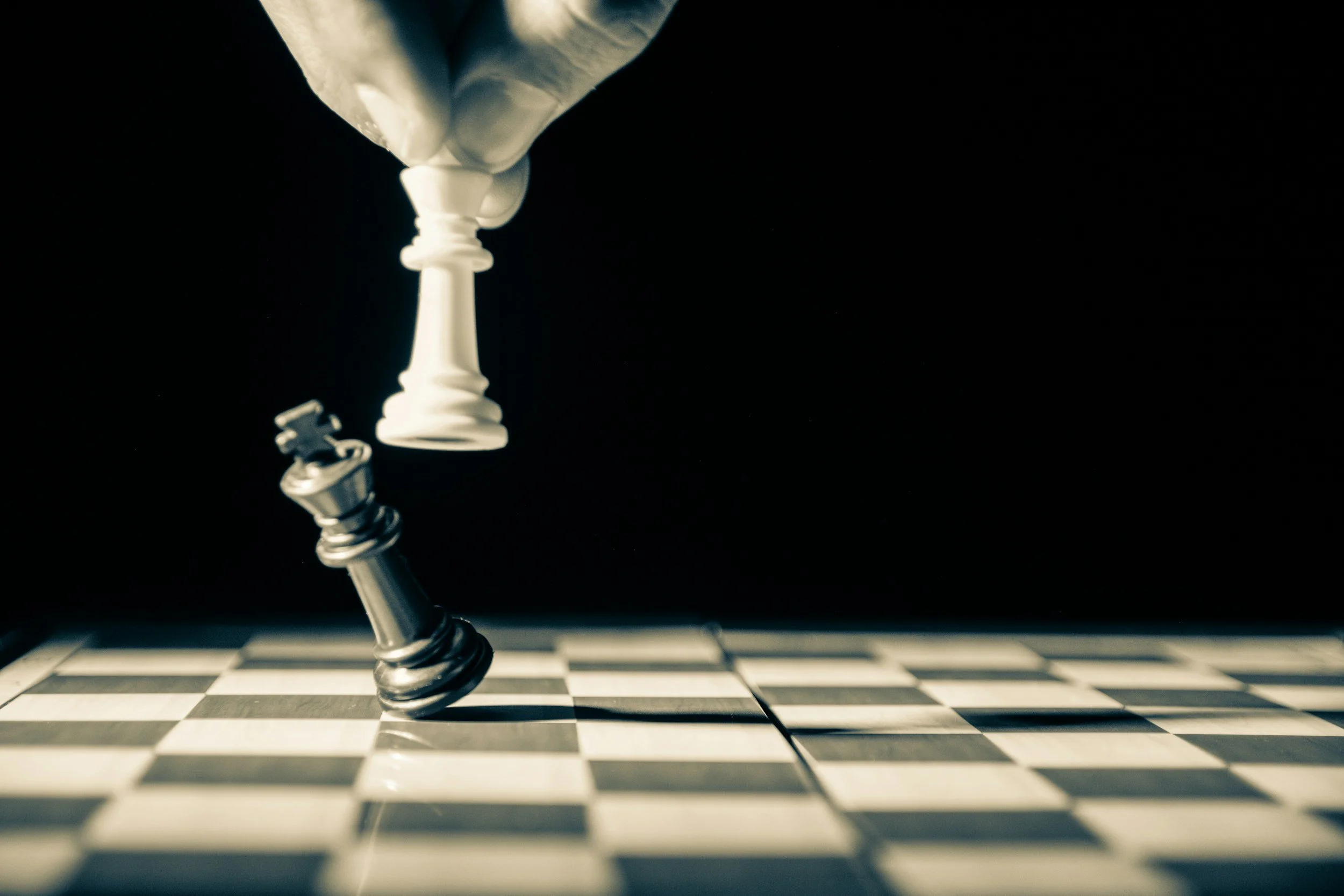 A close-up of a chess king piece and a pawn on a black and white checkered chessboard, with the king falling over.