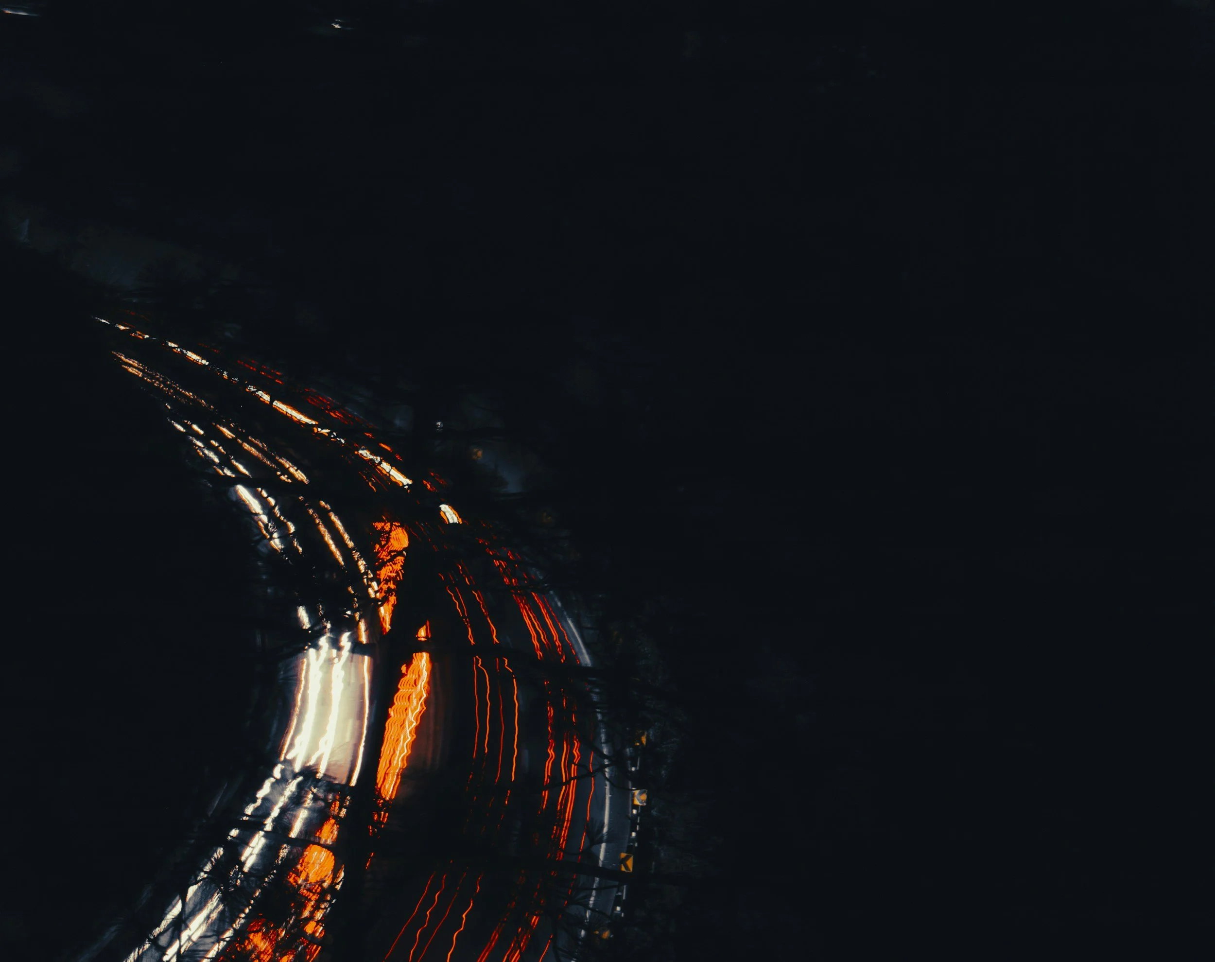 Nighttime image of blurred city lights and vehicle taillights creating streaks of orange and white light against a dark sky.