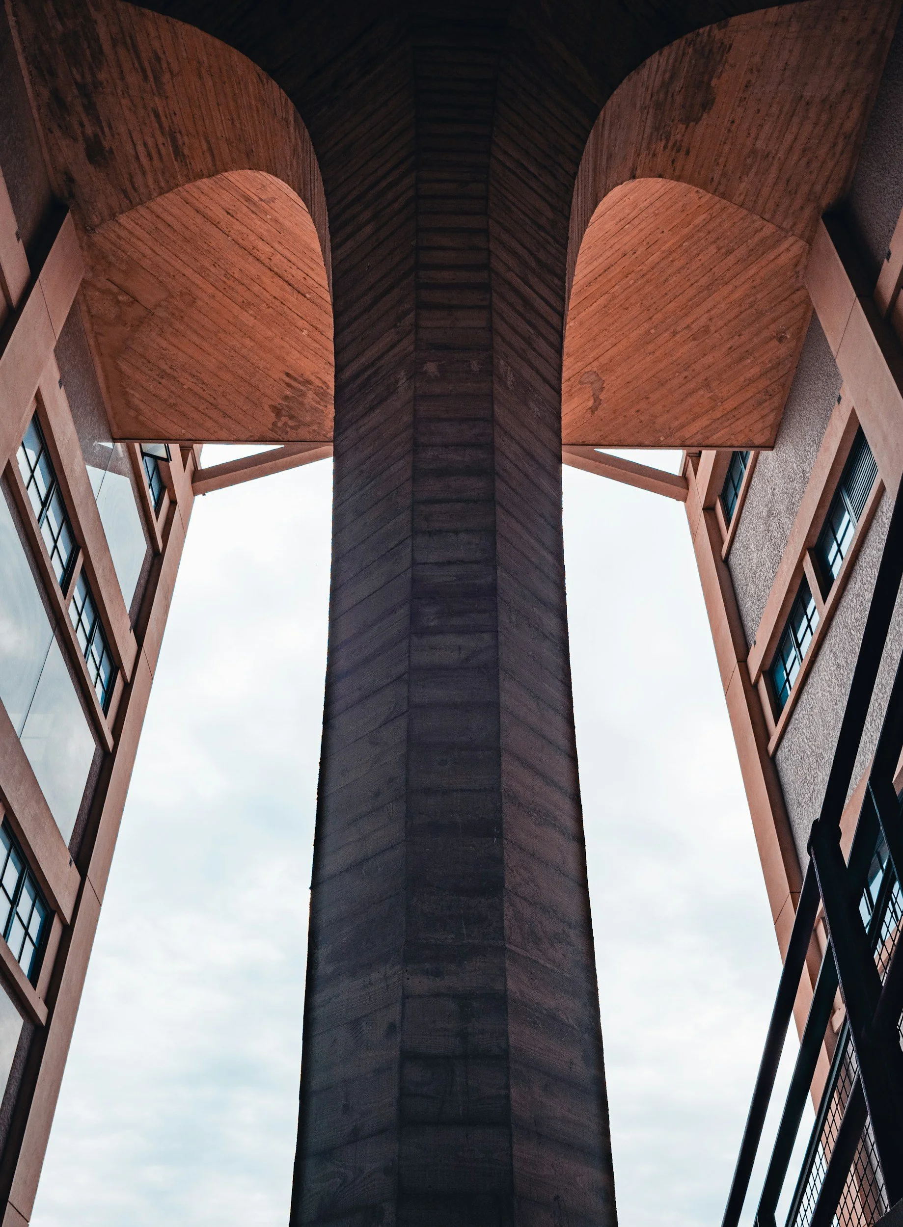 Looking up at a building's interior featuring exposed wooden beams and a central concrete or stone column, with windows and structures around.
